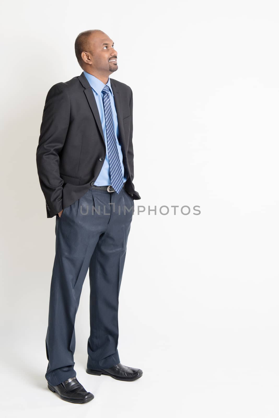 Indian businessman smiling and looking away towards copy space, full body standing on plain background.