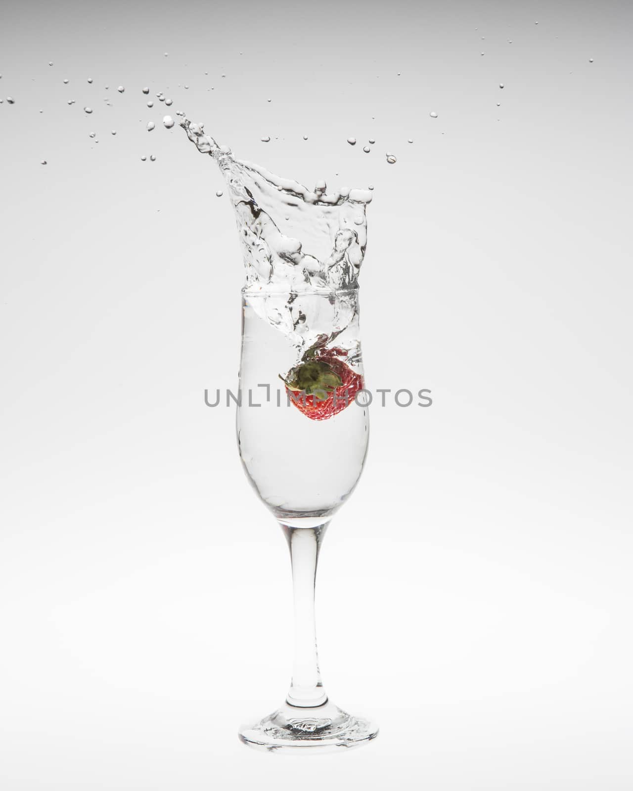 Strawberry falls deeply under water with a splash on white background
