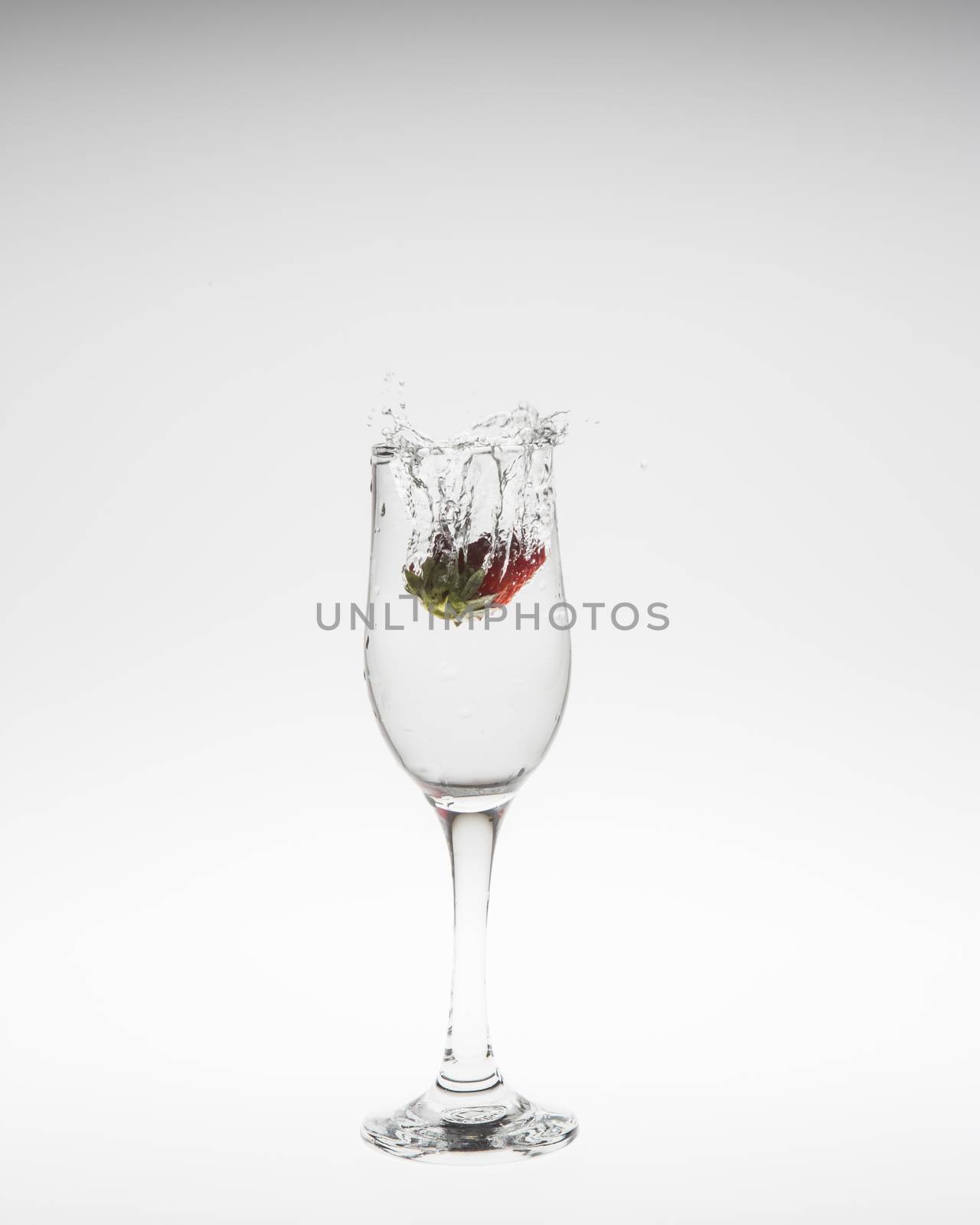 Strawberry falls deeply under water with a splash on white background