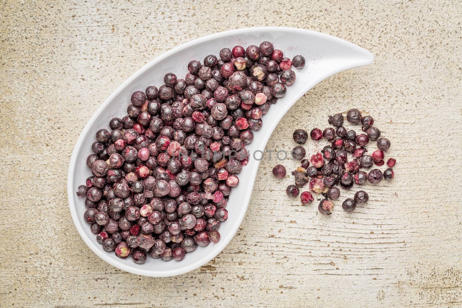 Freeze dried elderberries in a teardrop bowl against rustic barn wood. Elderberries are rich in antioxidants and minerals which make them perfect in battling the common cold.