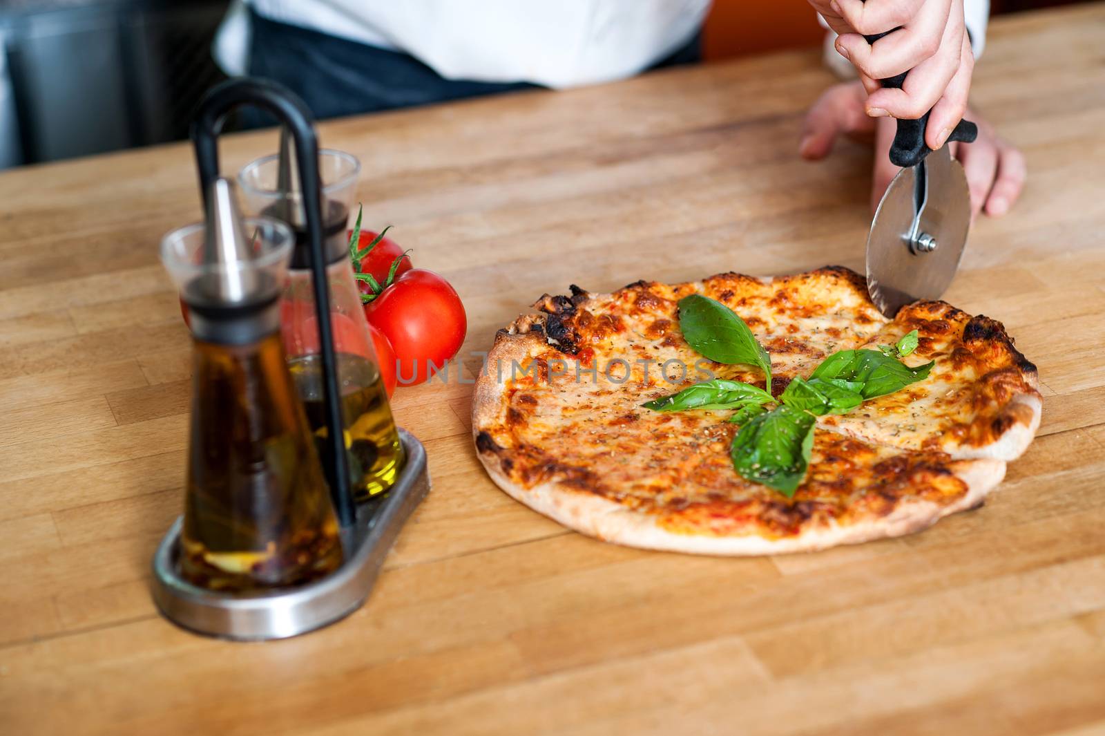 Baker cutting pizza at kitchen by stockyimages