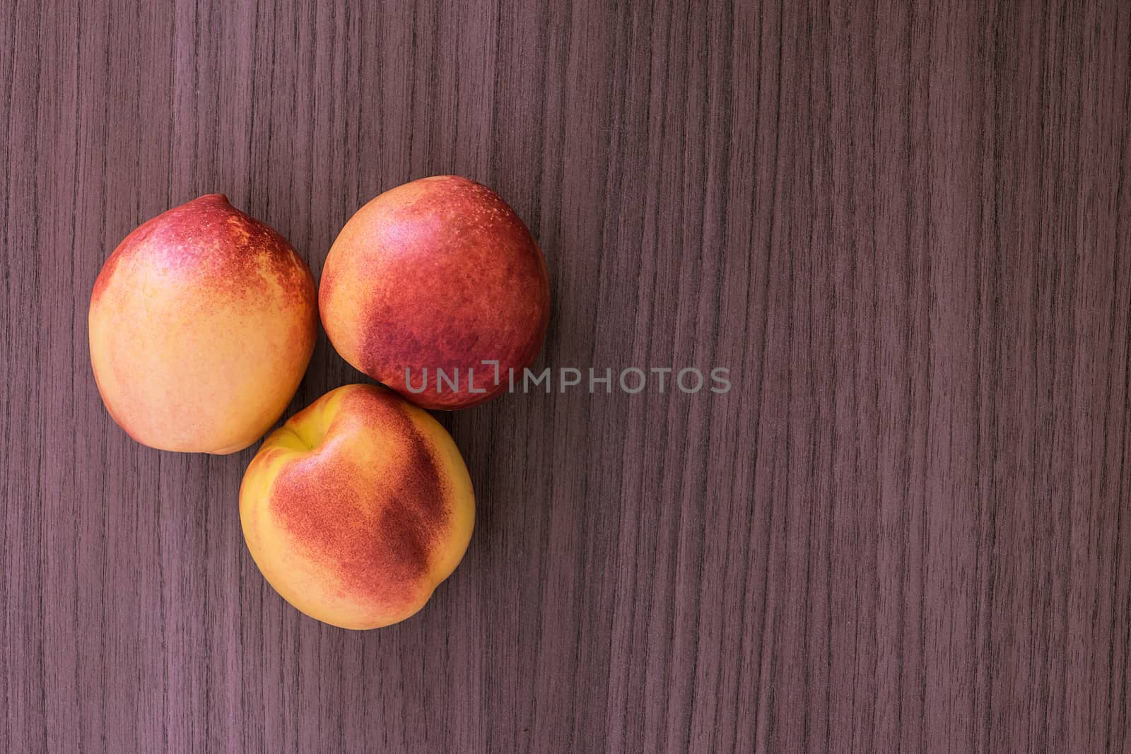 Three succulent red and yellow peaches over wood 