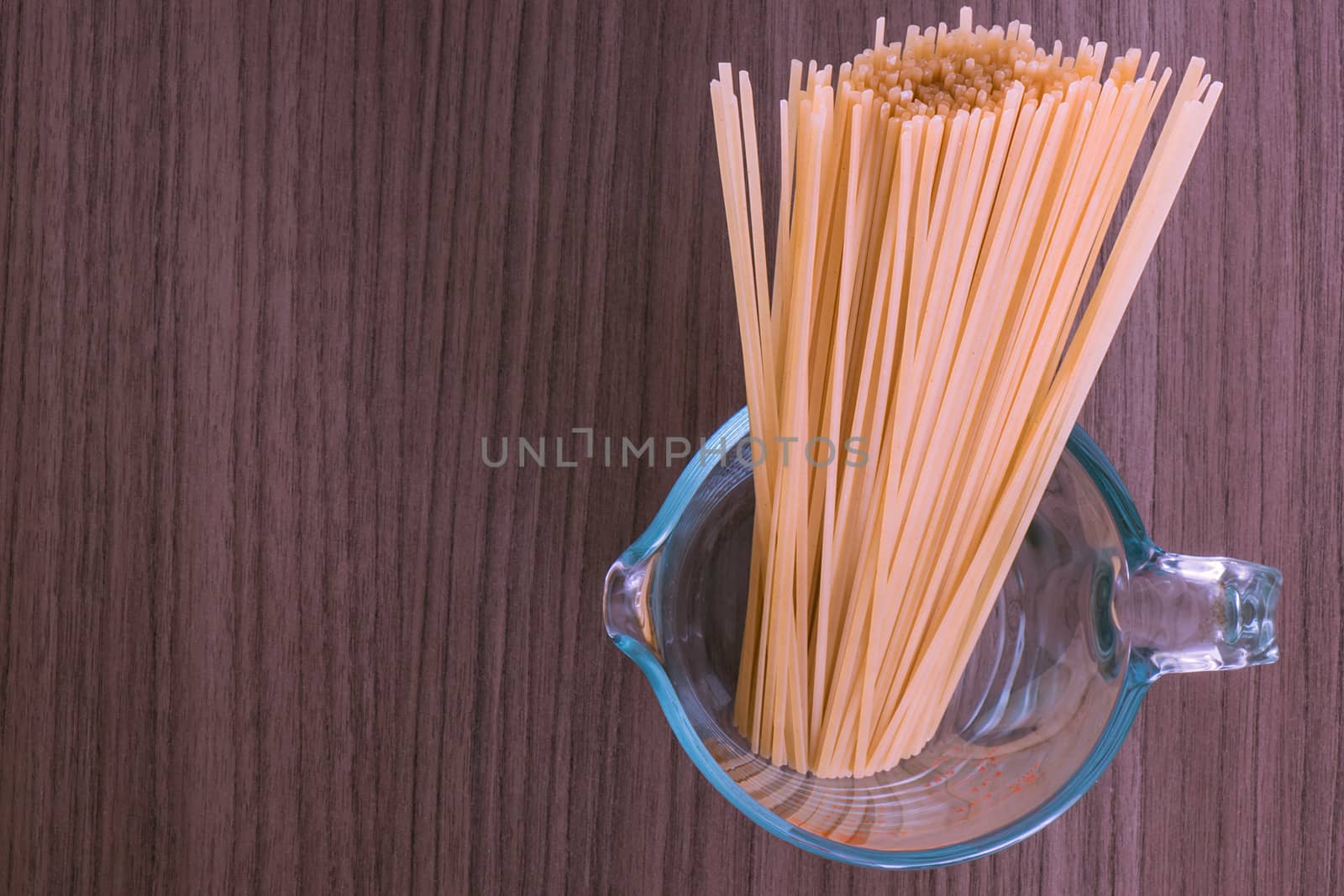 Some dry spaghetti into a glass container over wood 