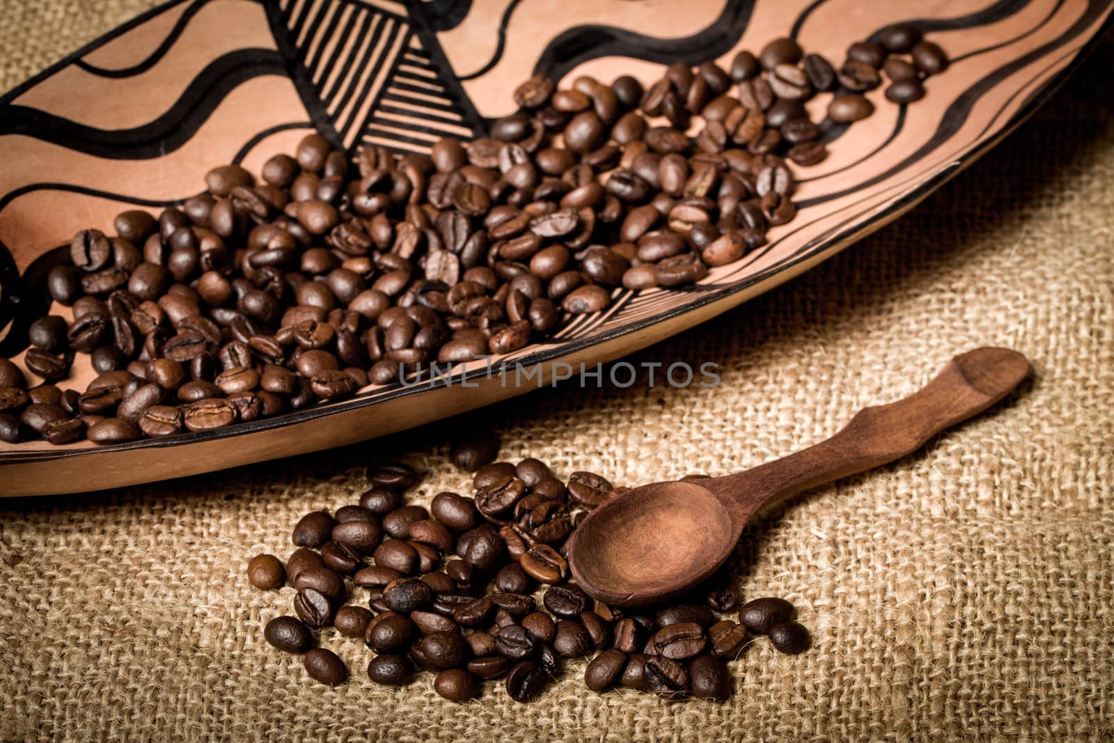 pile of fresh and bio aromatic coffee beans in african bowl and wooden spoon