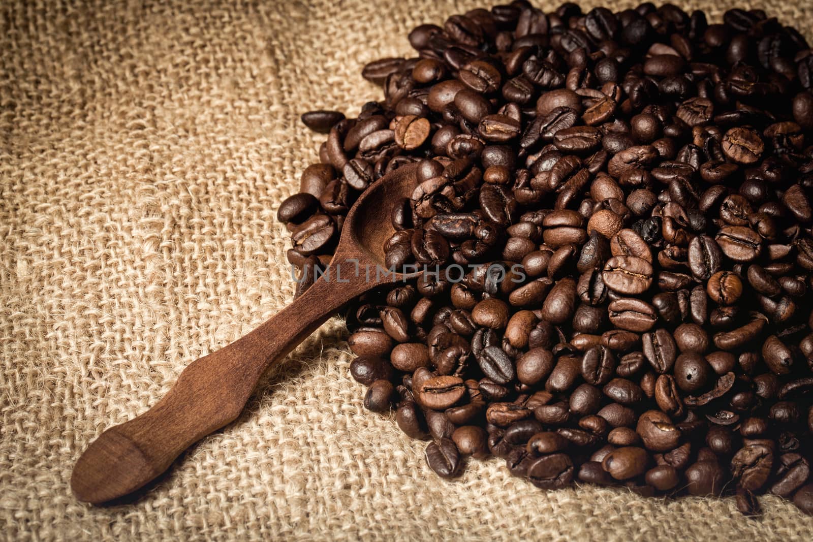 pile of fresh and bio aromatic coffee beans and wooden spoon