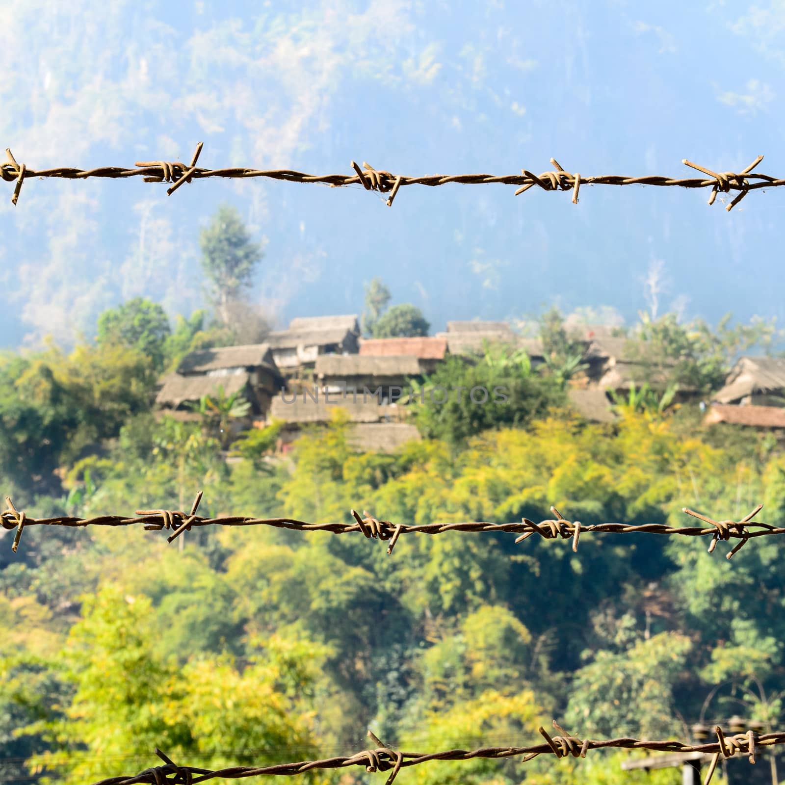 The Barbed Wire in front of Refugee House that made from Wood,Bamboo and Leaf Roof at Refugee Camps in the North of Thailand.