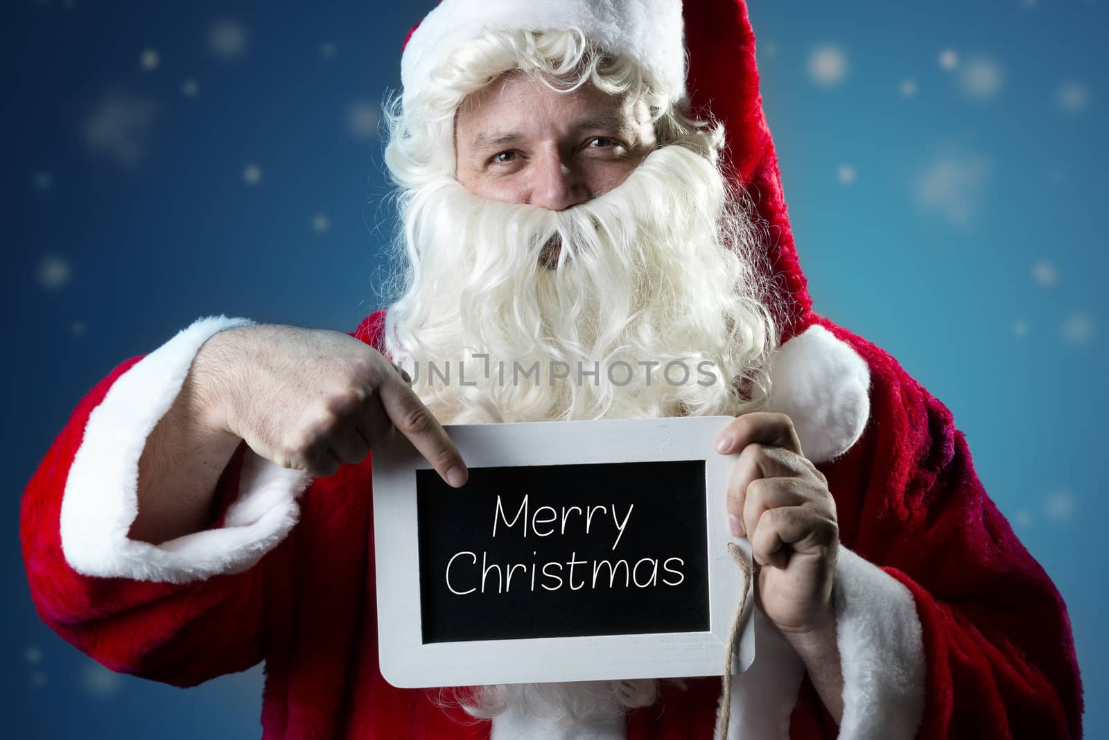 Santa Claus pointing a finger on a blank slate with text Merry Christmas