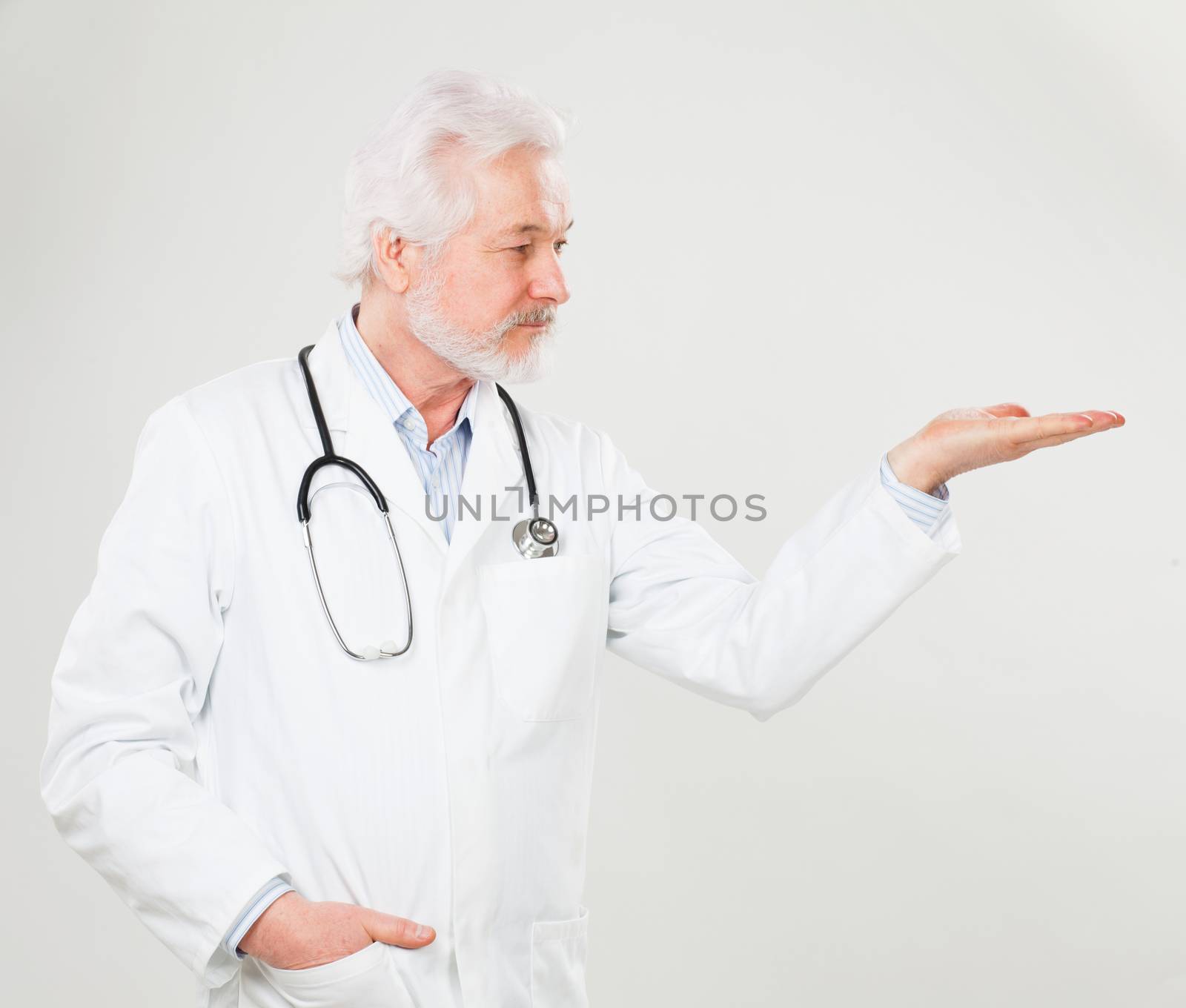 Handsome elderly doctor holds something on his hand over background