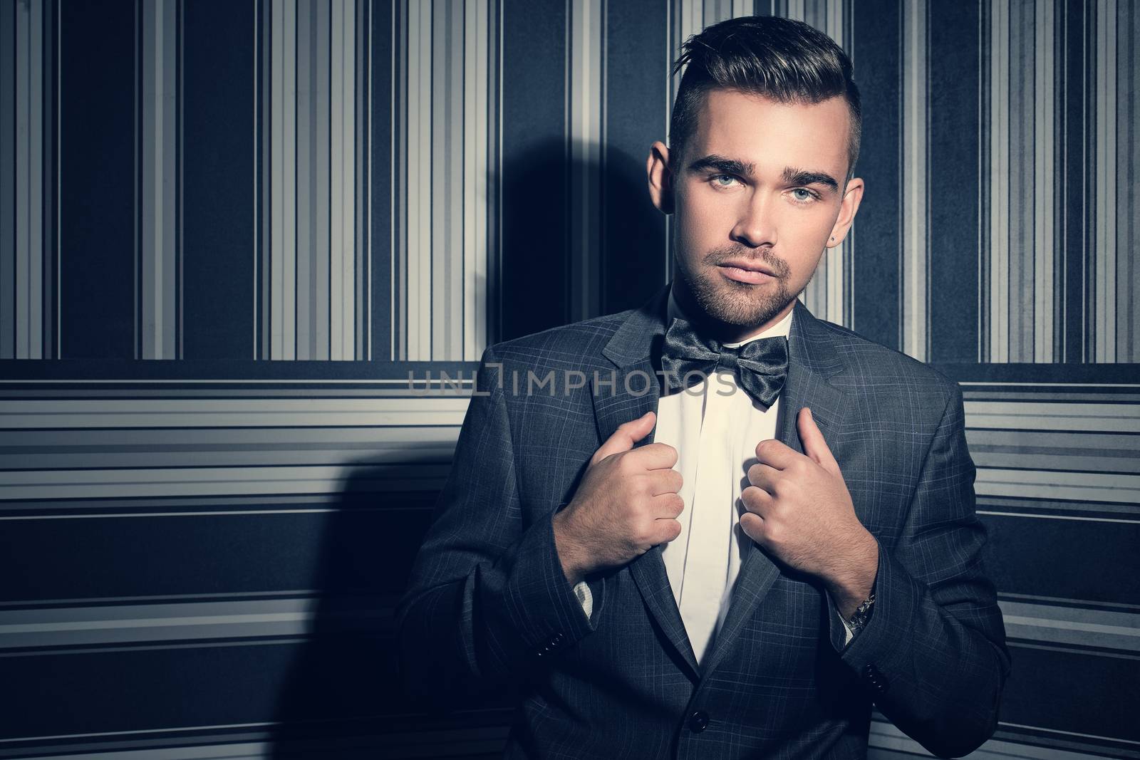 Portrait of a handsome man in a suit and a tie who is posing over a striped background