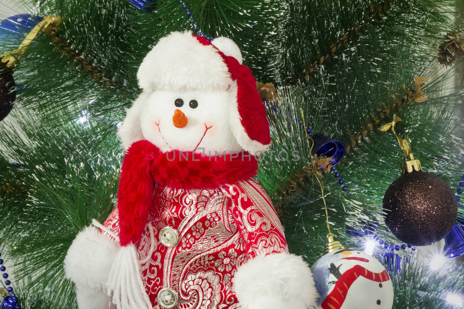 Snowman in a red cap and elegant clothes against the decorated Christmas fir-tree