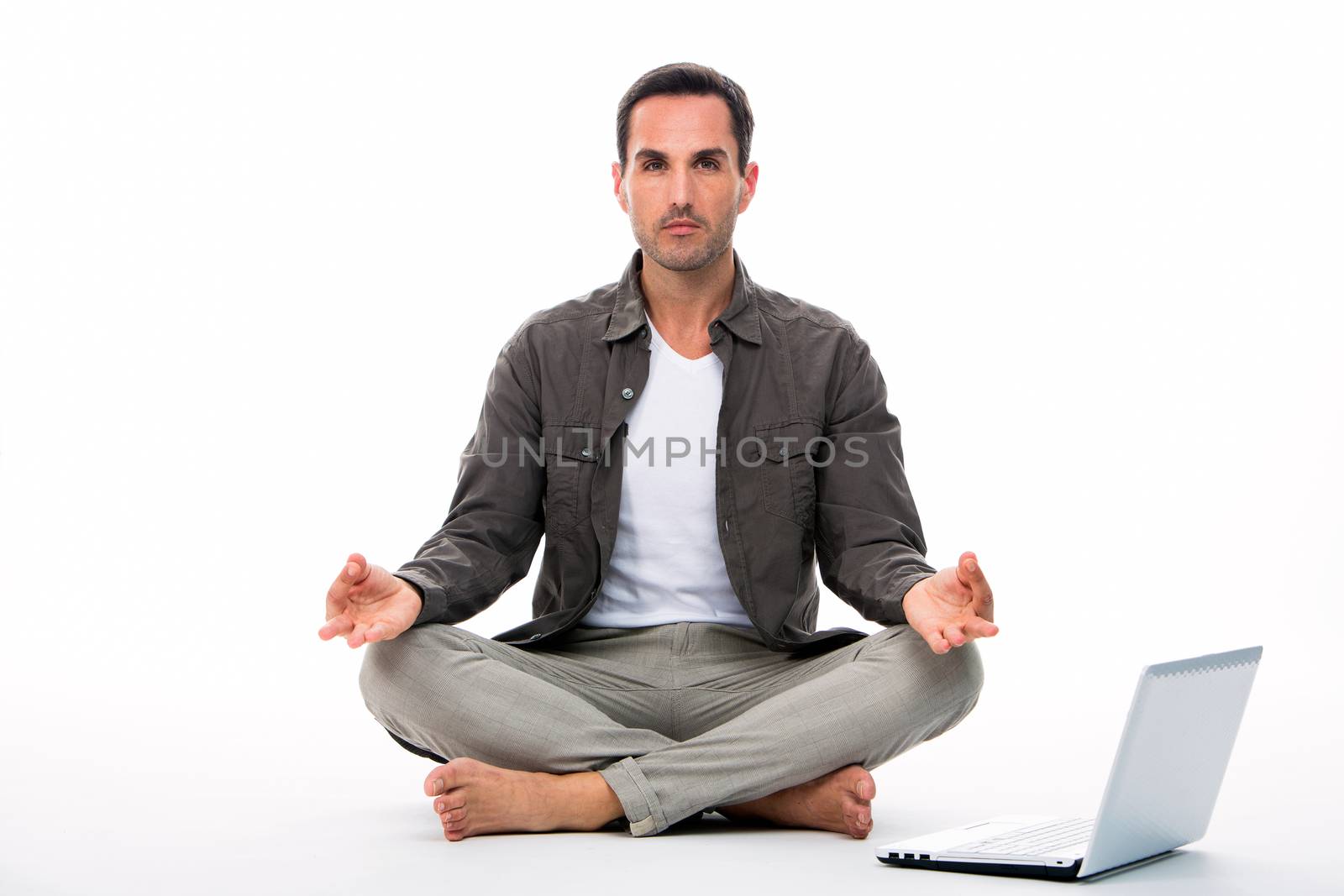 Man sitted on the floor looking at the camera and practicing yoga with laptop next to him