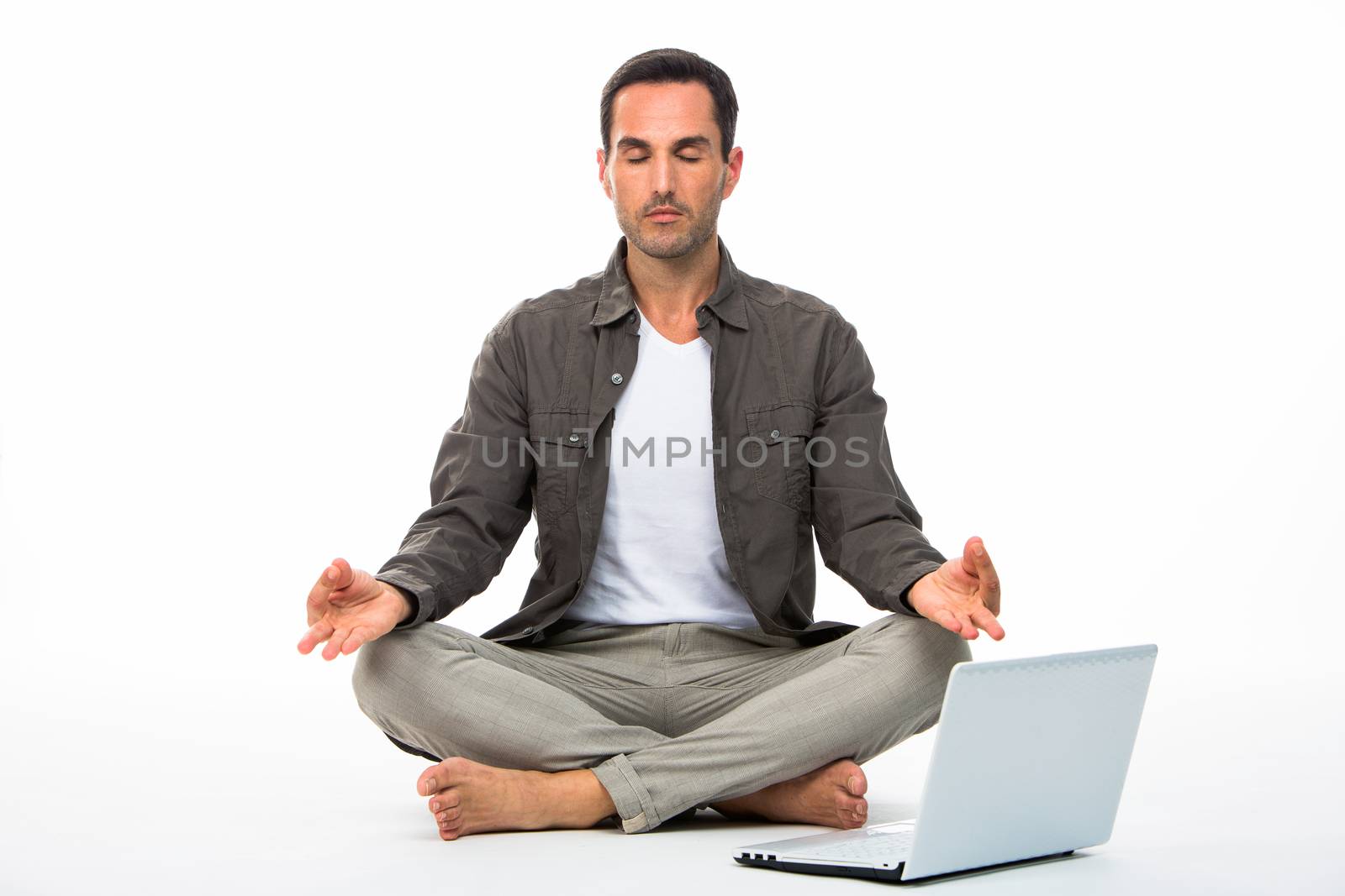 Man sitted on the floor with eyes closed practicing yoga with laptop next to him