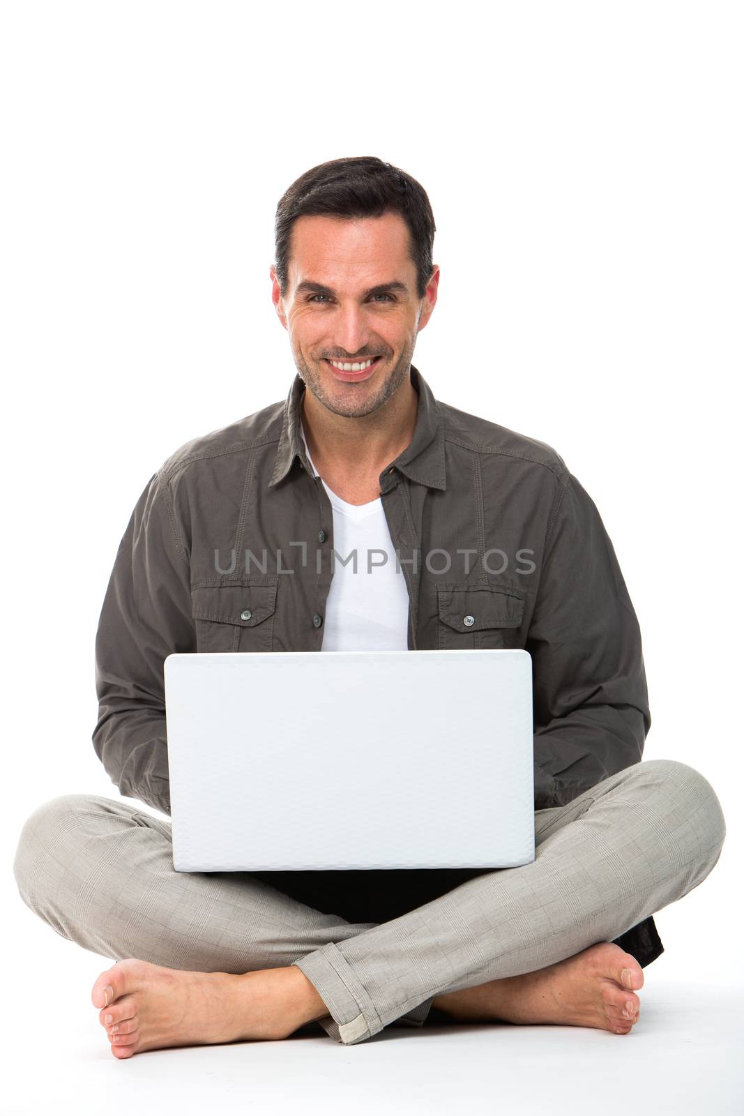 Man sitted on the floor, smiling at camera and working with his laptop