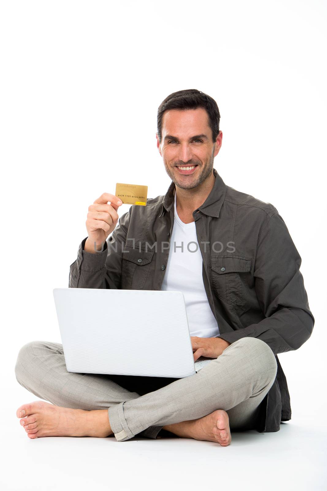 Man sitted on the floor, smiling at camera, showing credit card and buying online