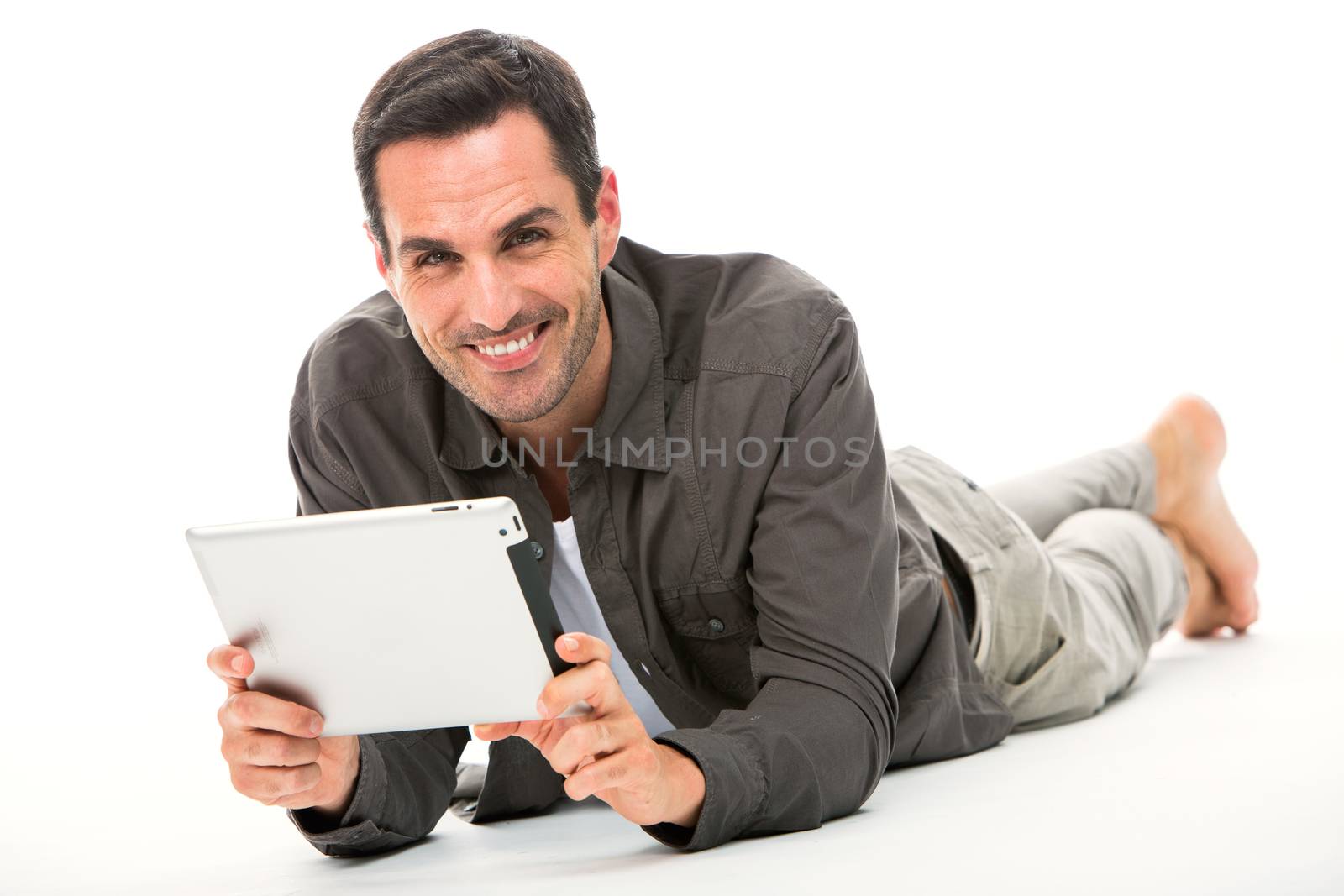 Man laying on the floor, smiling at camera and holding his digital tablet with both hands