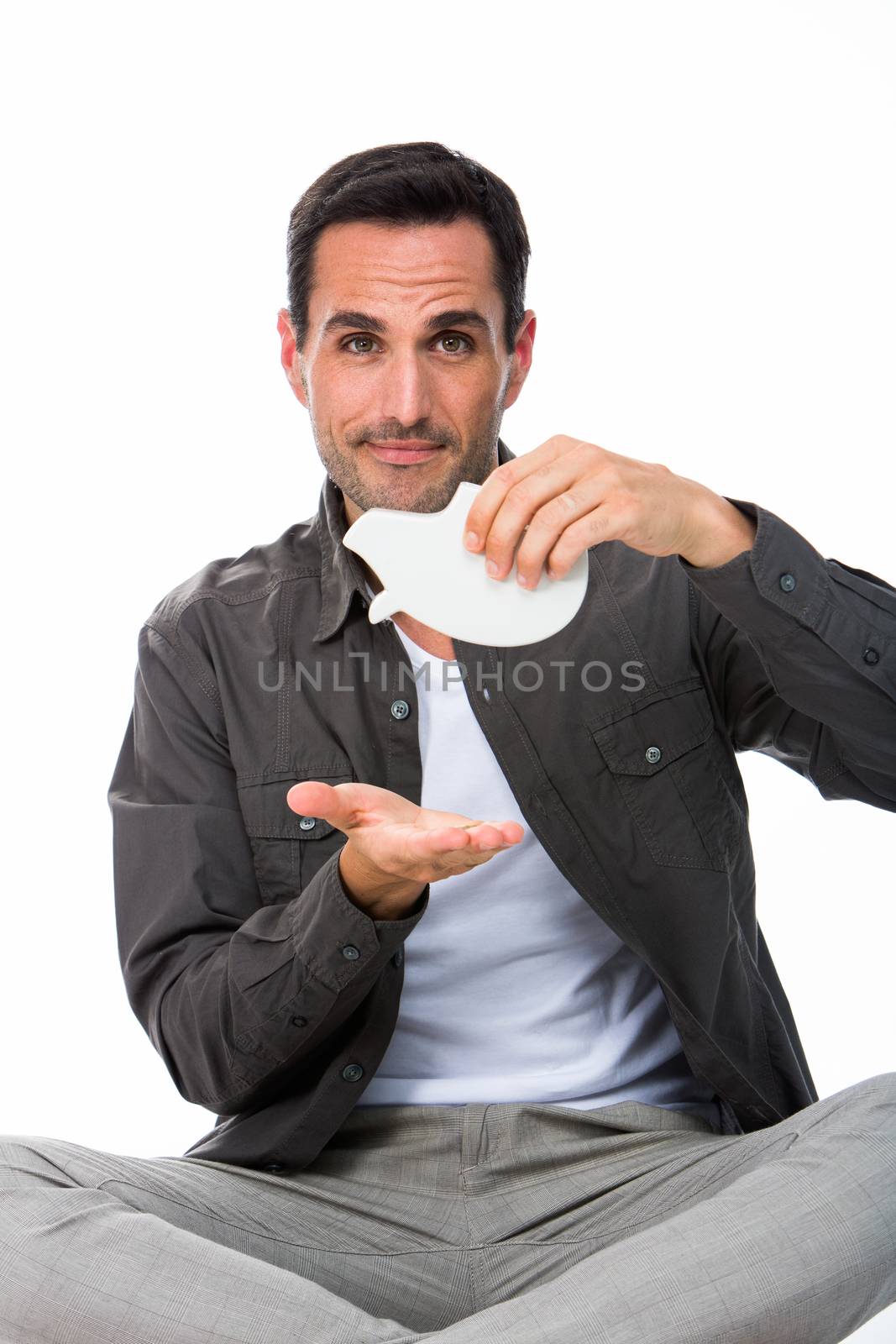 Man sitted on the floor, looking at camera and showing an empty piggy bank