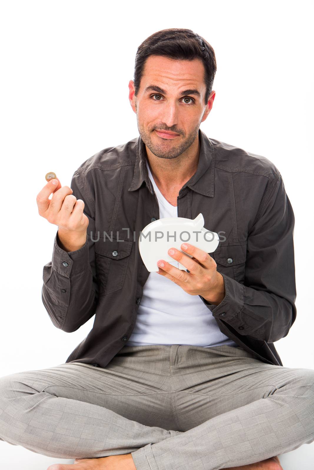 Man sitted on the floor, looking at camera, putting a coin in a piggy bank