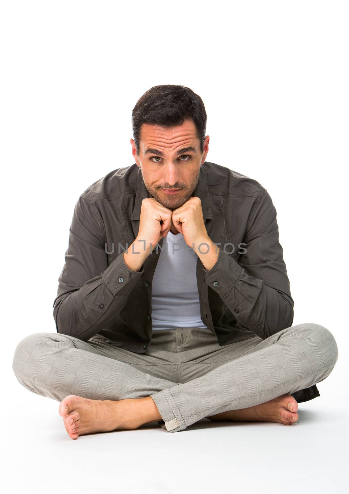 Thoughtful man sitted on the floor, looking at camera, with the hands under his chin