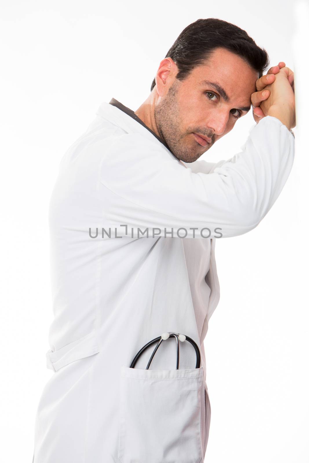 Half length profile portrait of a thoughtful male doctor, looking at camera, his hands leaning to a wall