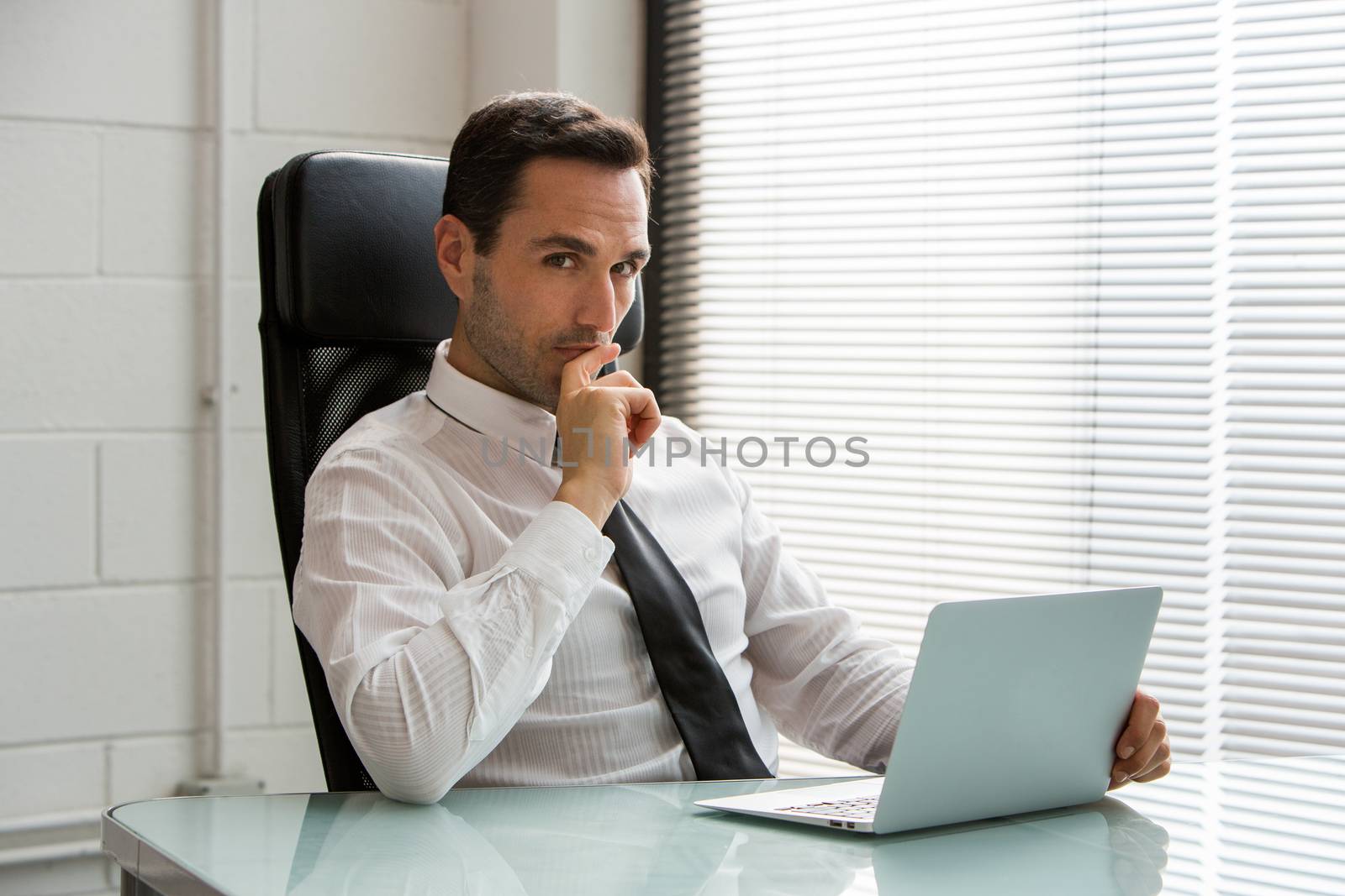 Half length portrait of a thoughtful male businessman, looking at camera and working with a laptop computer