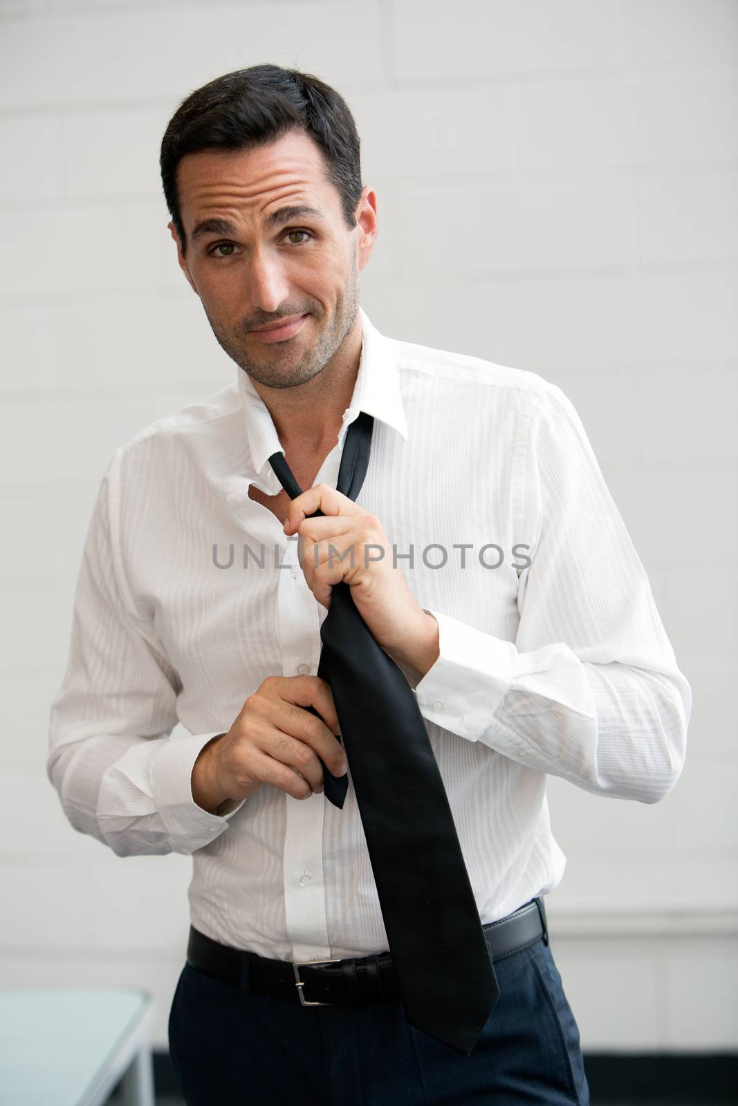 Half length portrait of a businessman looking at camera while taking off his tie