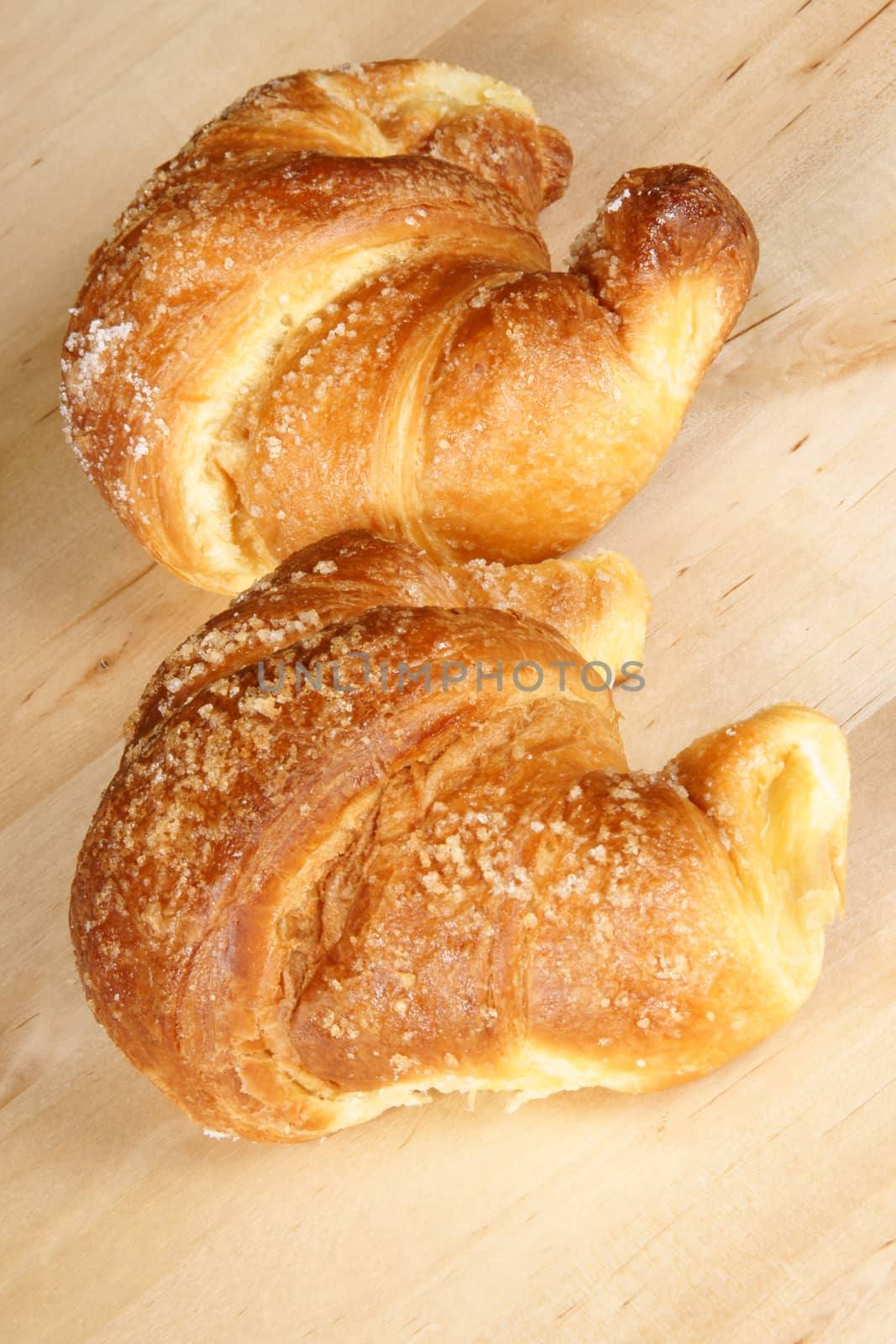Two freshly baked croissants with granulated sugar over a wooden table