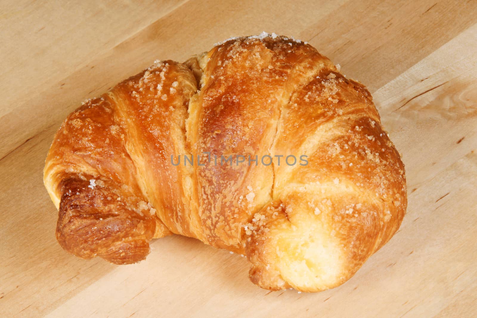 Freshly baked croissant with granulated sugar over a wooden table