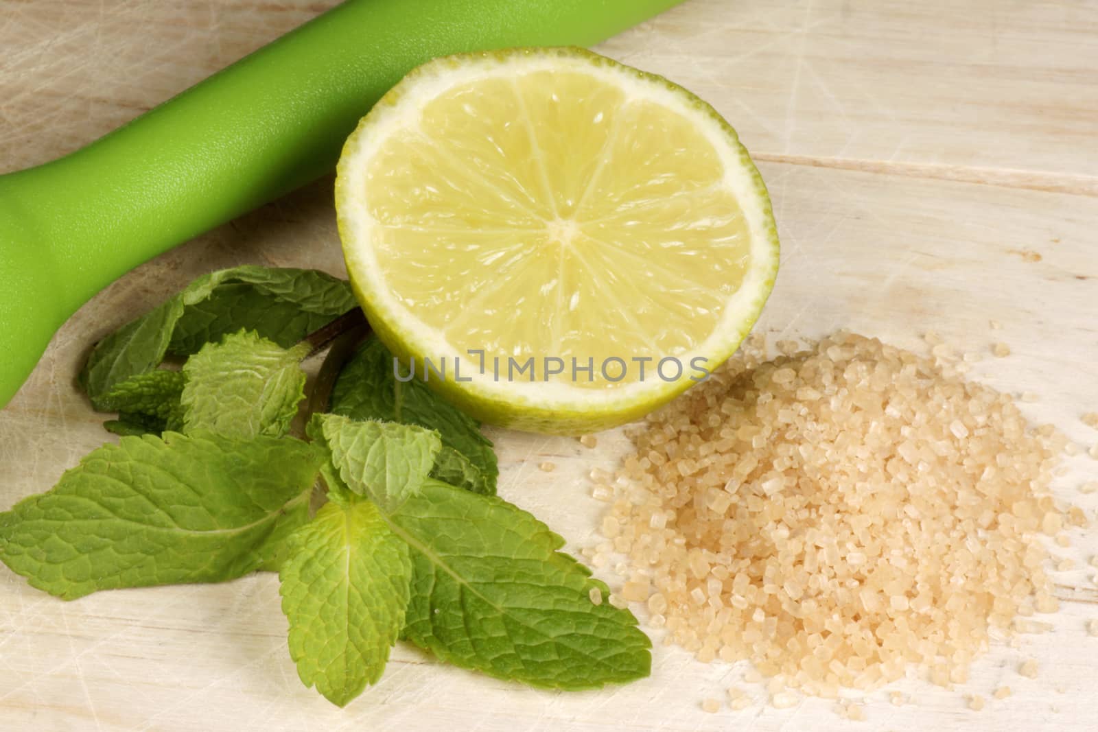 Half cut lime, sugarcane, spearmint leaves and a muddler on a wooden background ready to make a mojito cocktail.