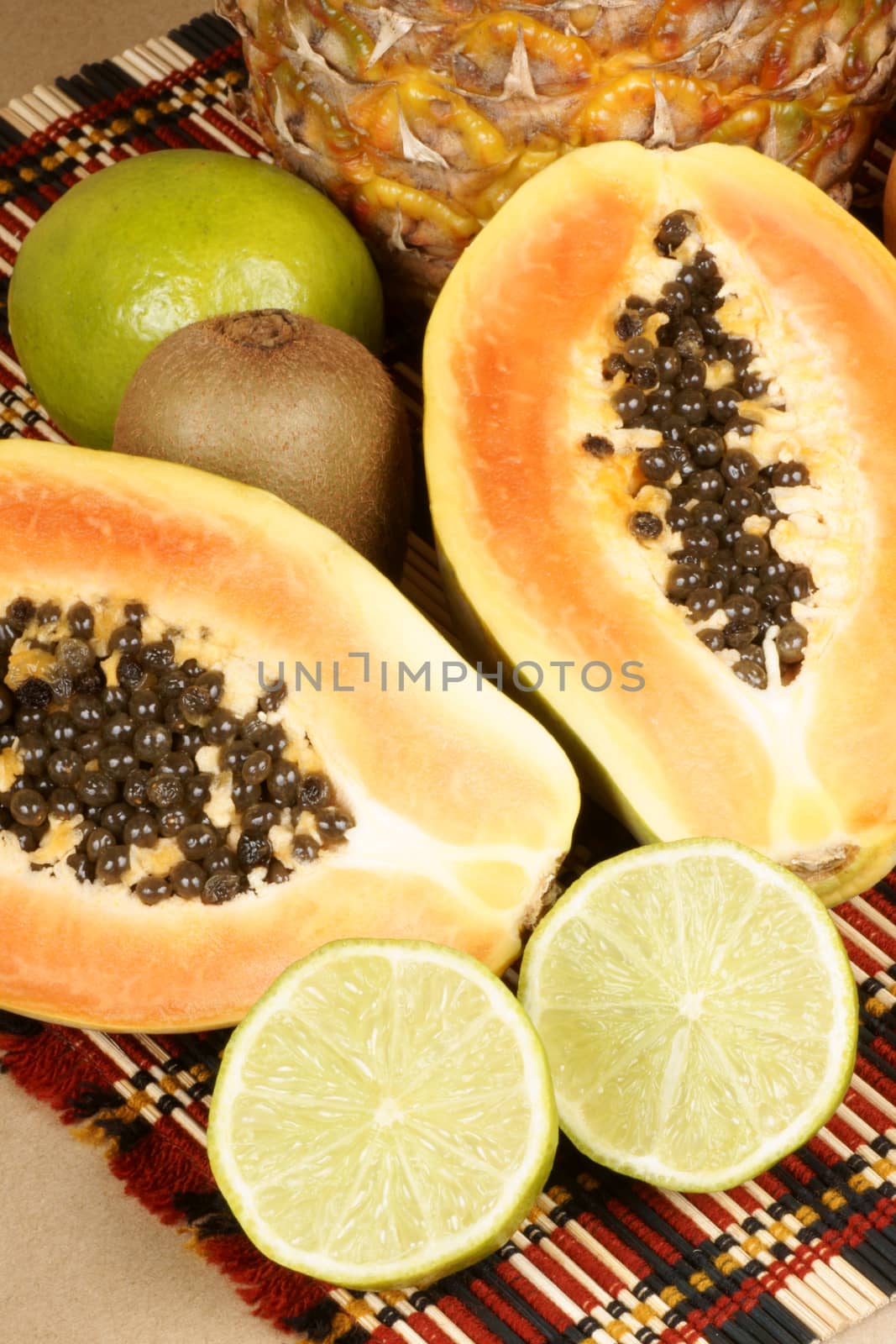 Tropical fruit composition with a half cut papaya, lime, pineapple and kiwi