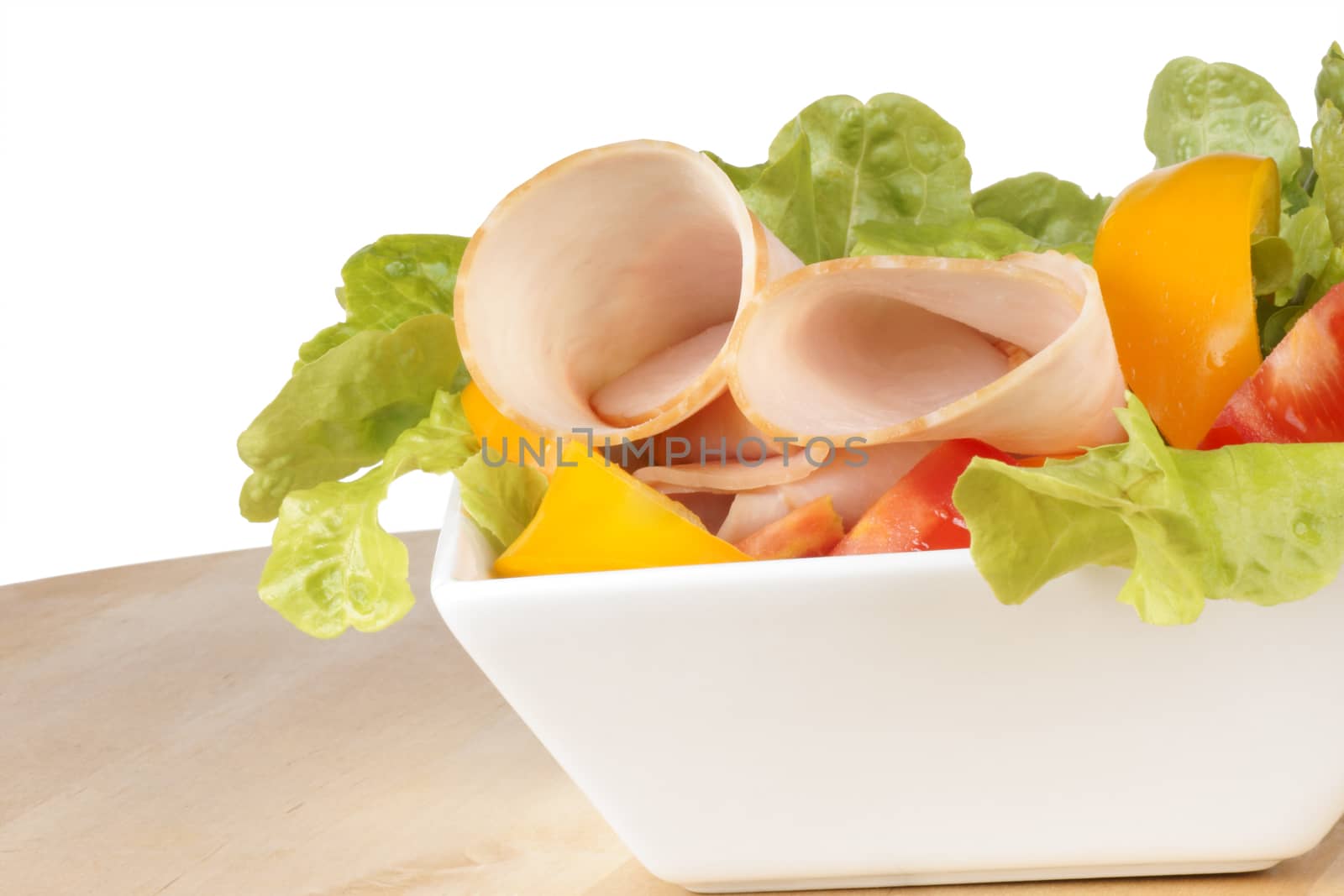 Close-up of a mixed salad with lettuce, tomatoes, bell peppers and roast turkey over a wooden cutting board. Over white background with copy space.