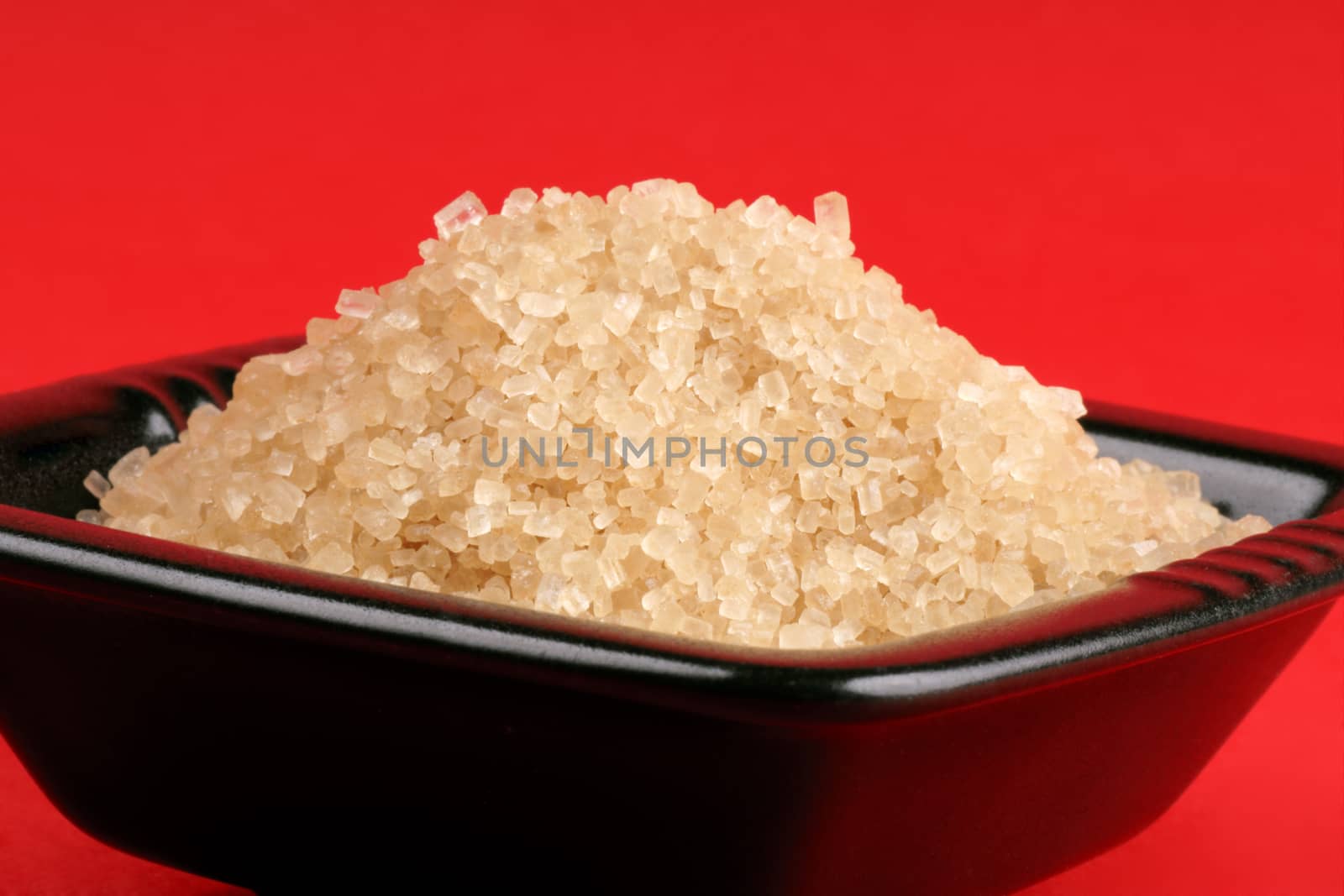 Brown sugar in a black bowl over a red background.