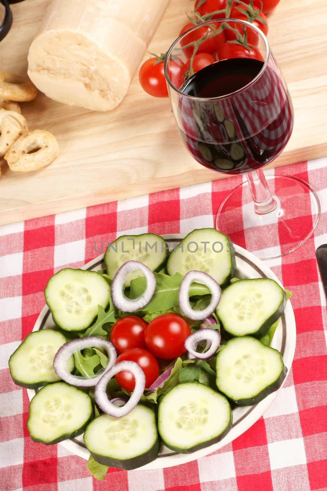 Close-up of a prepared table with an healthy salad, a glass of red wine, fork and knife. In the background some red tomatoes and parmesan cheese. Selective focus.
