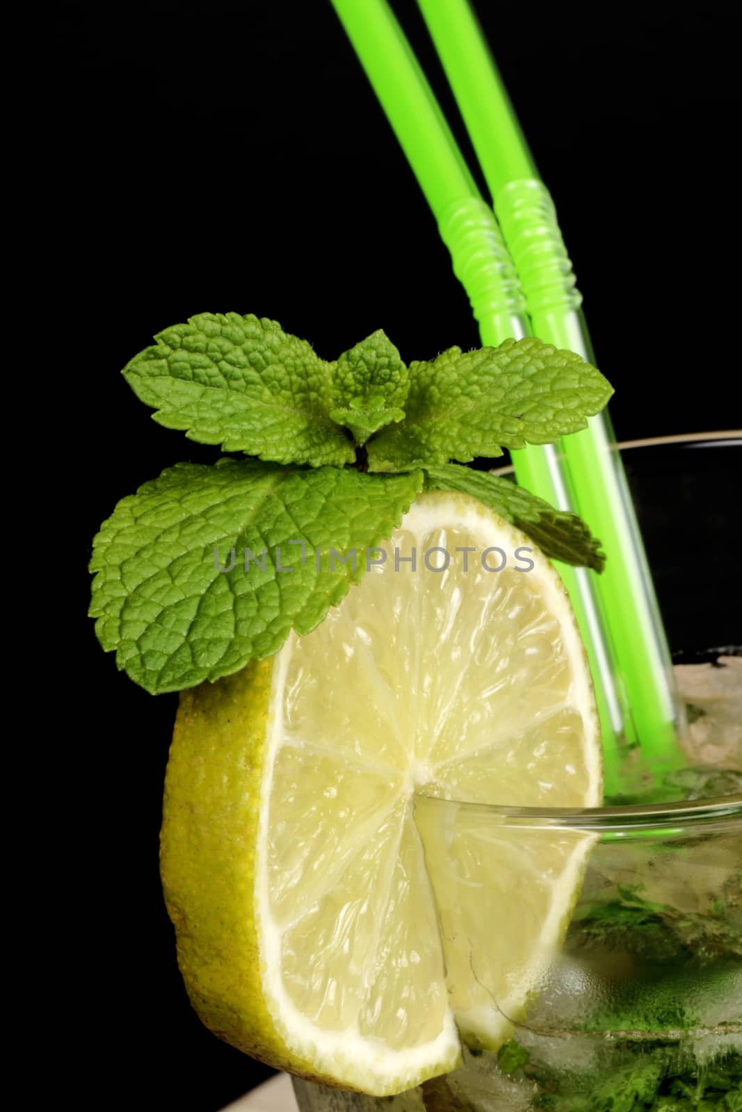 Close-up of a Mojito cocktail with two straws over black background