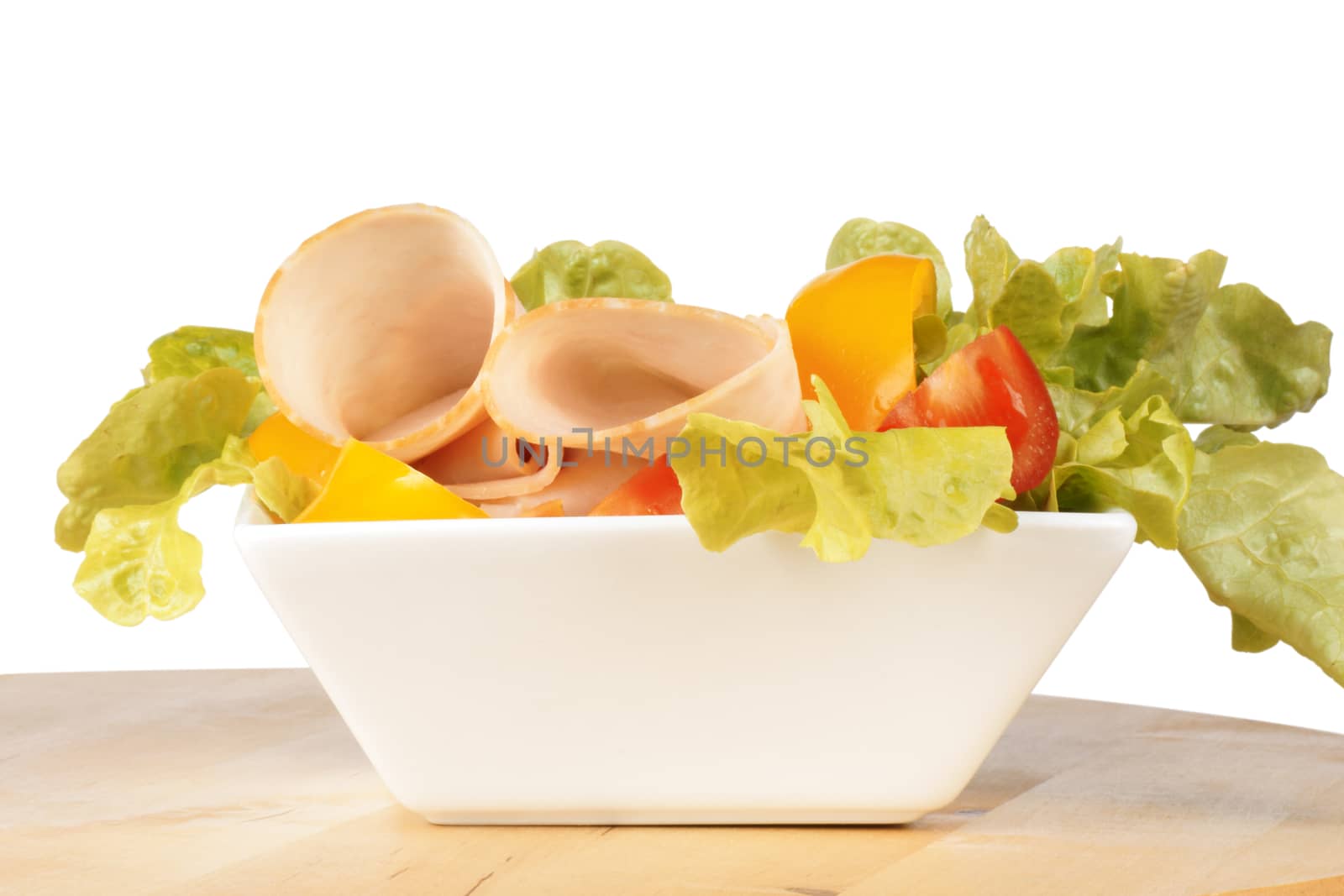 Close-up of a mixed salad with lettuce, tomatoes, bell peppers and roast turkey over a wooden cutting board. Over white background with copy space.