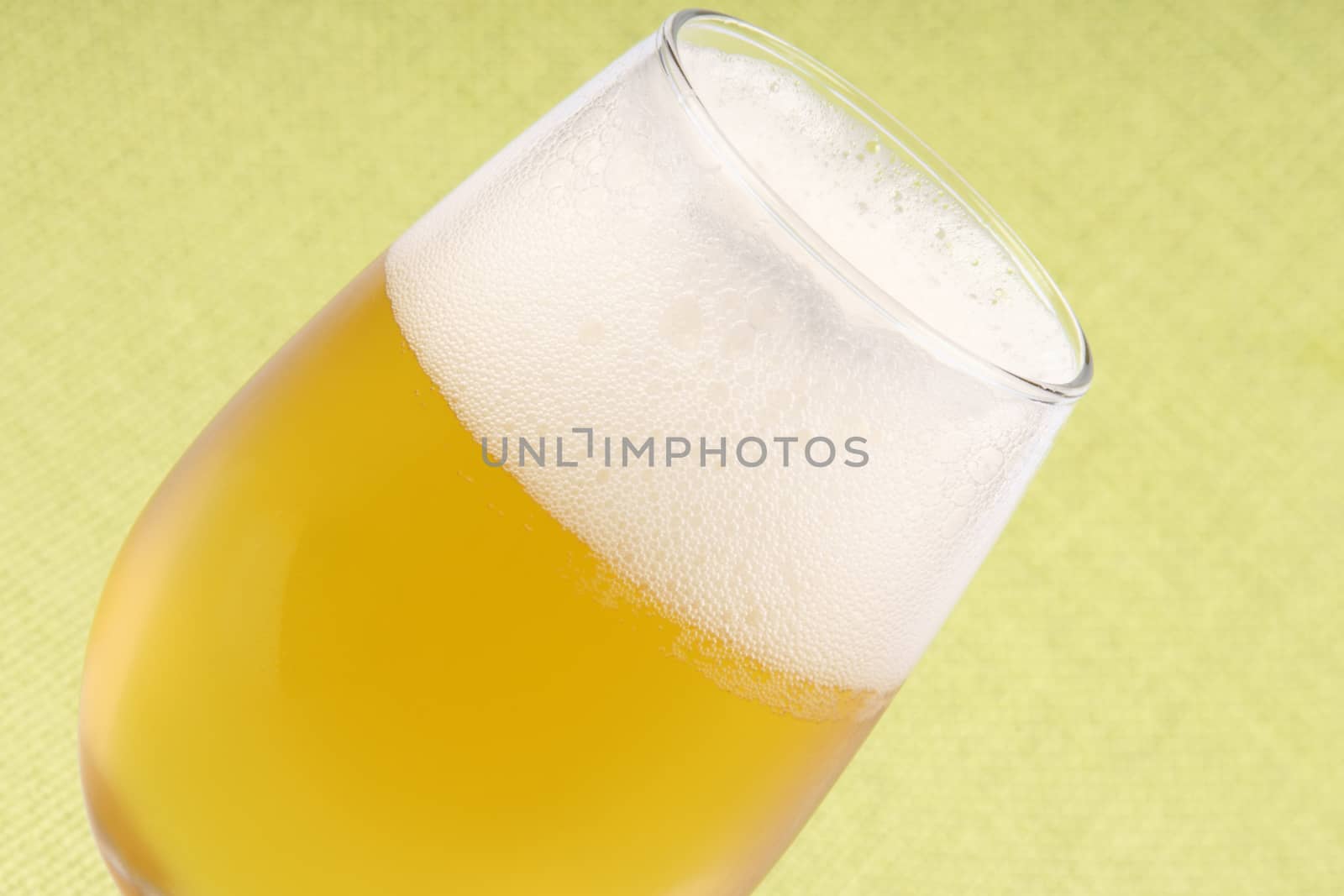 Close-up of a glass of cold pale lager beer over a light green background.