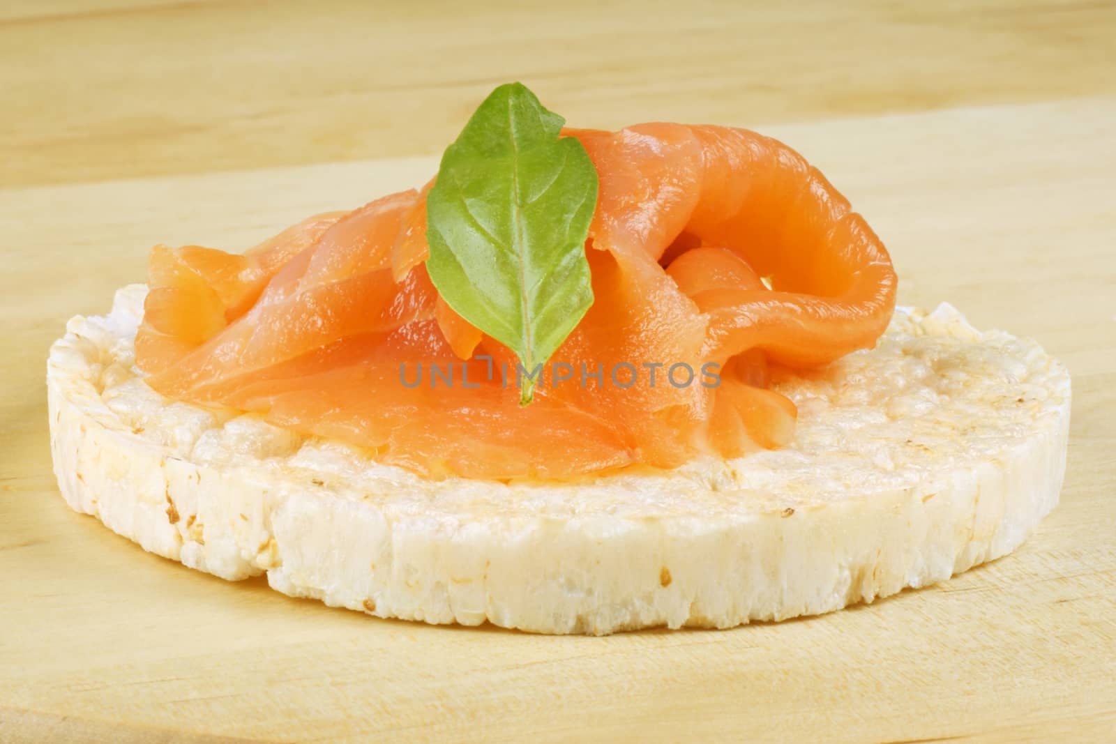 Close-up of a rice cake with smoked salmon and basil, over a wooden background.