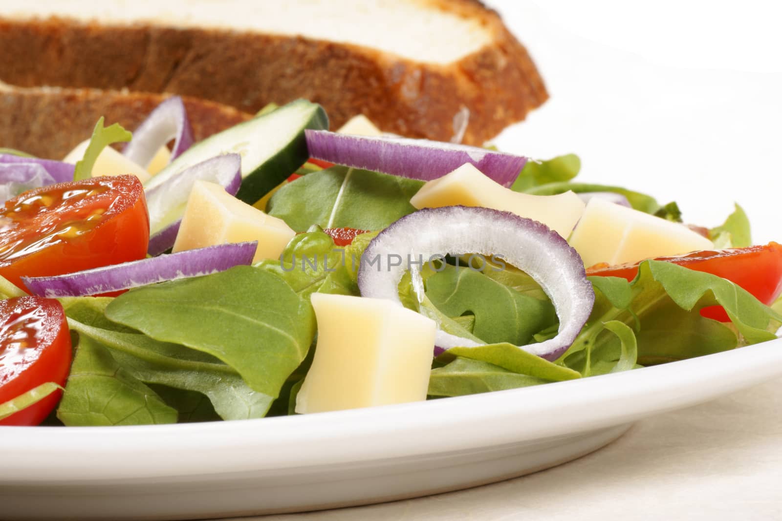 Close-up of an healthy mixed salad with cheese and slices of bread in the background. Selective focus.