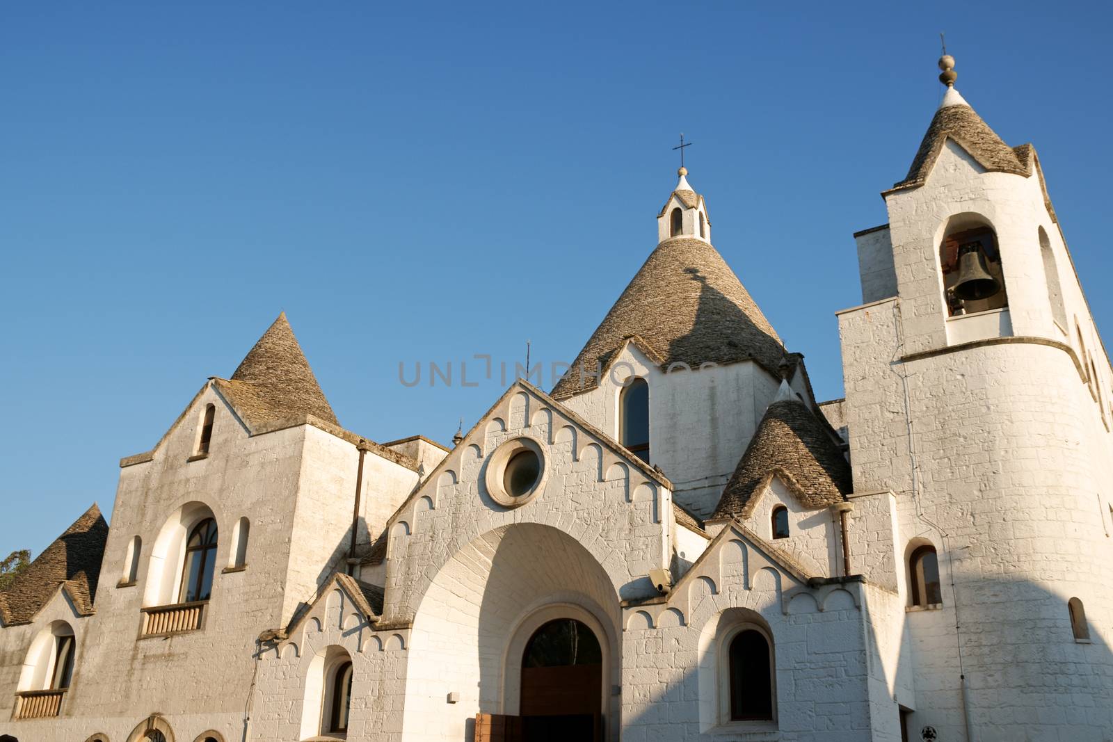 San Antonio trullo church in the sunset light. Alberobello was founded in the 15th century on land that was originally an oak forest in the province of Bari. A typical feature of Alberobello are the trulli, white dry-stone houses with conical roofs made of lapidary stones. In 1996, Unesco made the town of Alberobello a world heritage site.