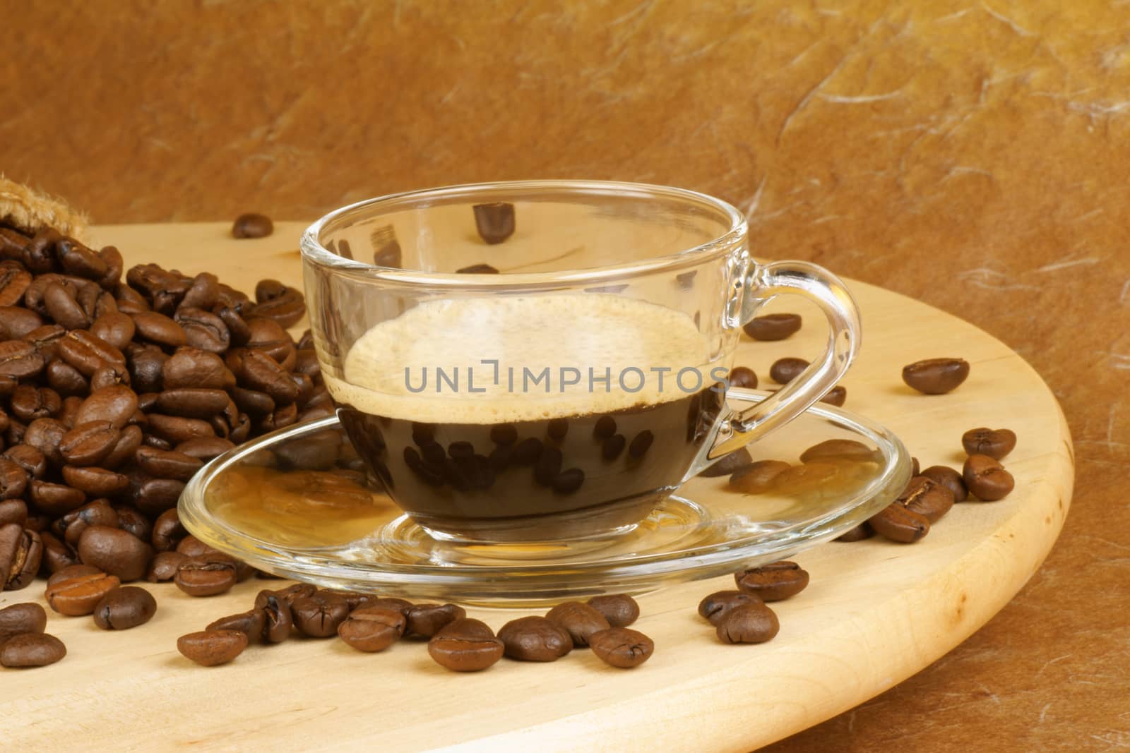 Close-up of a glass cup with italian espresso over a wooden table, surrounded by coffee beans.