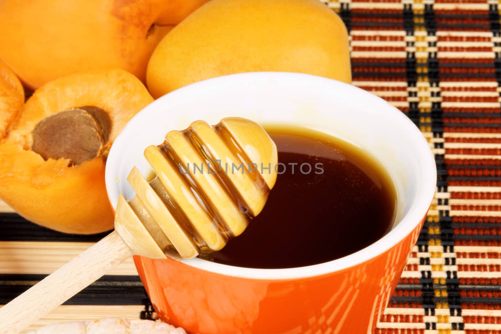 Close-up of honey in an orange pot with wooden dipper and apricots. Selective focus.