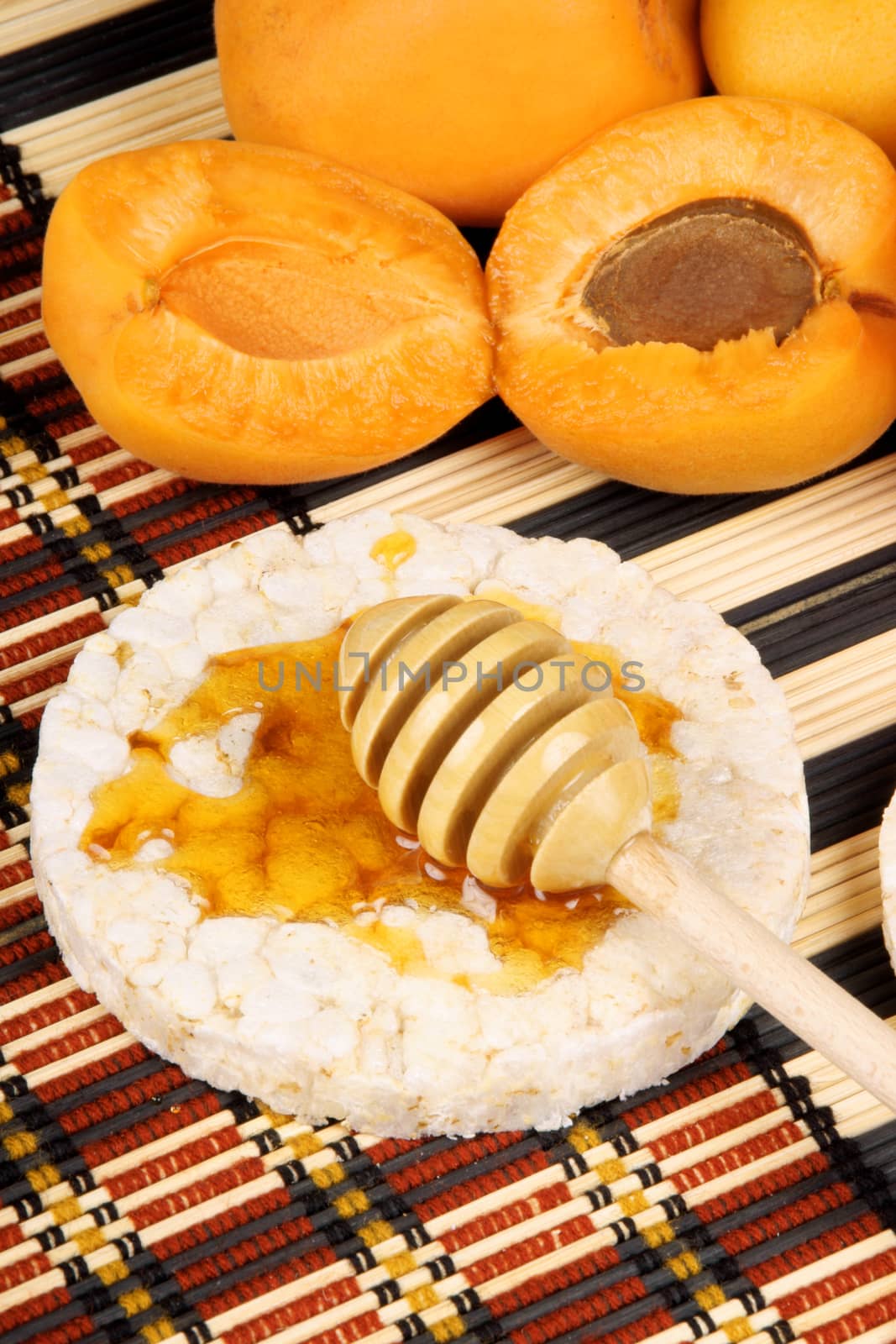 Close-up of rice cake with honey, wooden honey dipper and apricots. Selective focus.