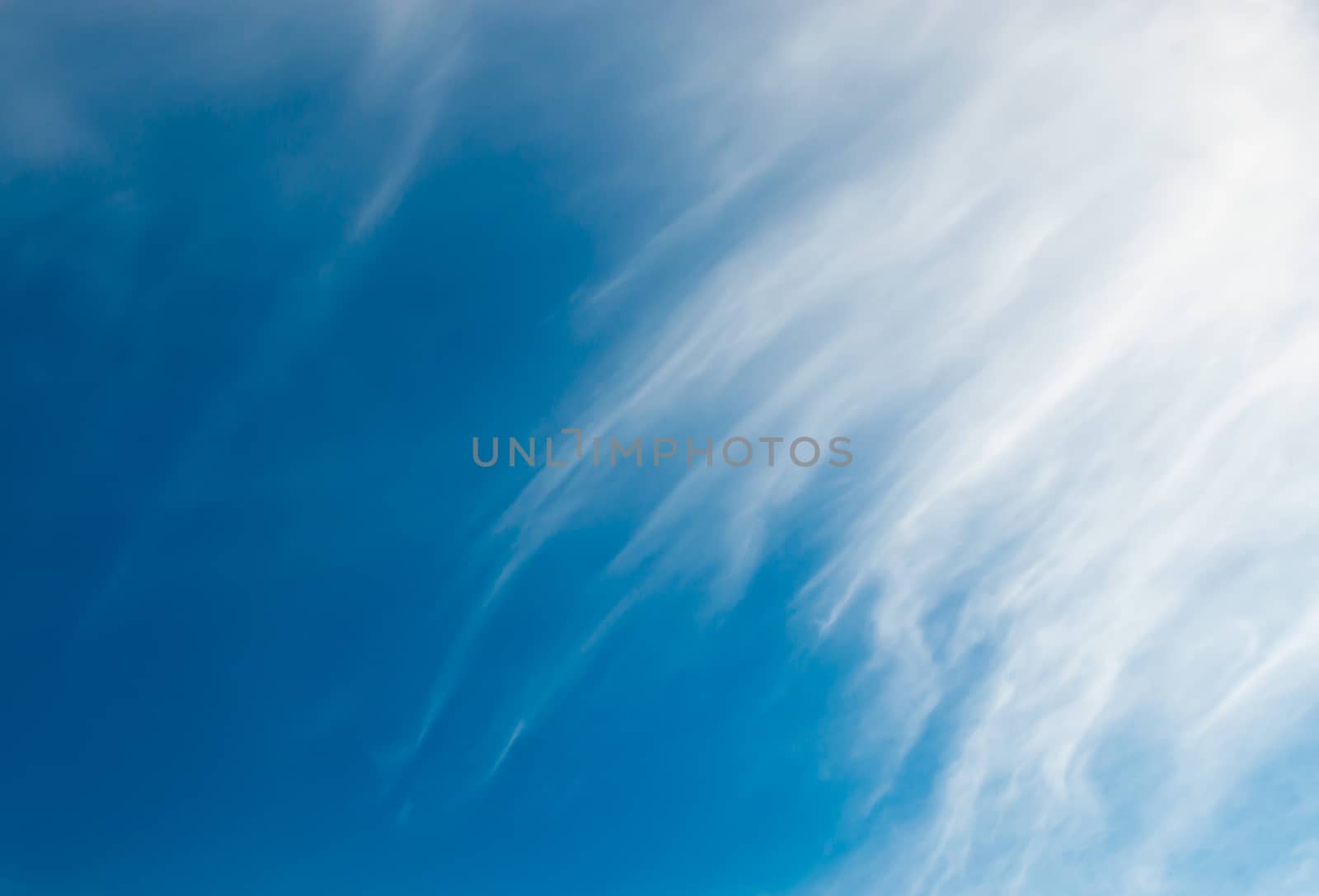 Cloud ad space background. Flighty cirrus clouds covering half the image, the other half is blue.