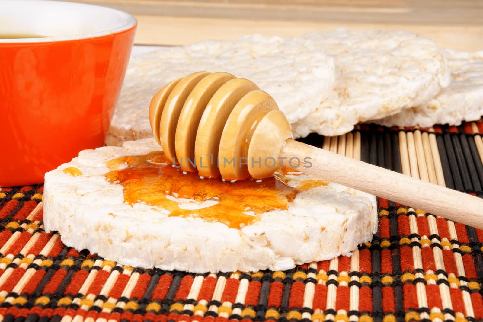 Close-up of a wooden honey dipper with honey on a rice cake