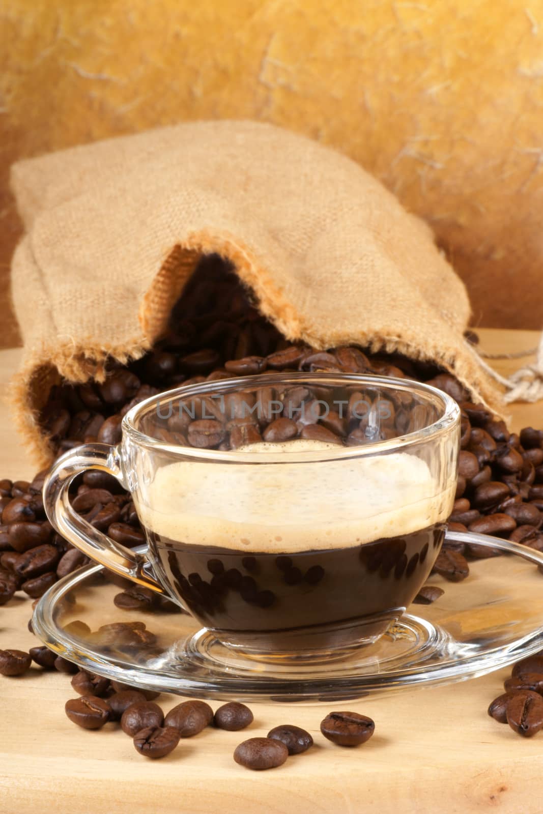Close-up of a glass cup with italian espresso over a wooden table, surrounded by coffee beans.