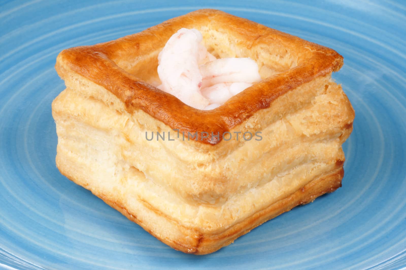 Close-up of a squared vol-au-vent stuffed with small boiled shrimps on a blue plate