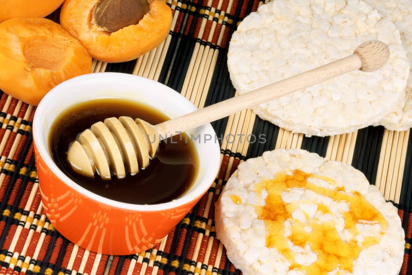 Close-up of honey in an orange pot with wooden honey dipper and apricots. Selective focus.