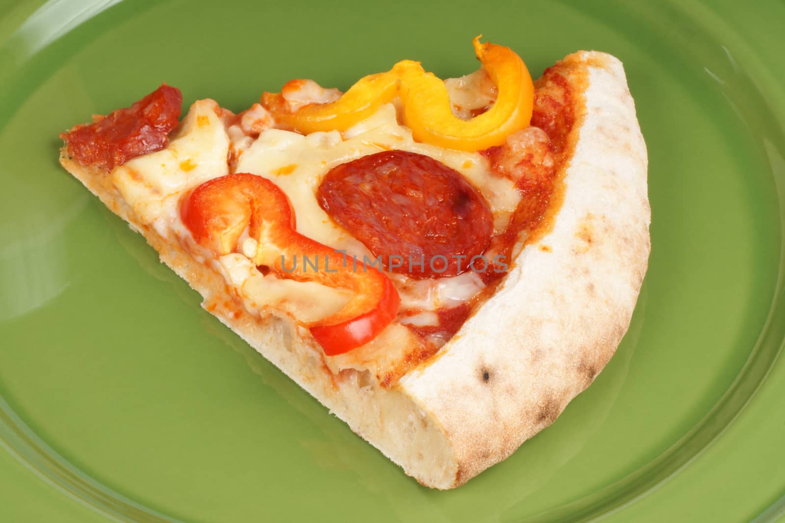 Slice of hot spicy pizza with mozzarella, tomato, salami and bell peppers served on a green dish