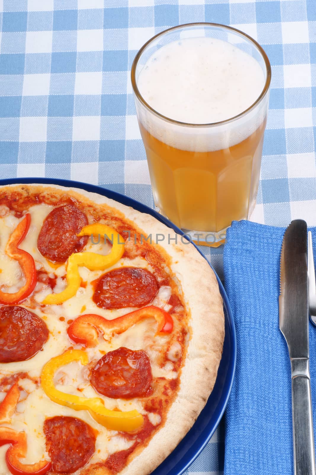 Set table with hot spicy pizza with salami and bell peppers and a glass of beer.