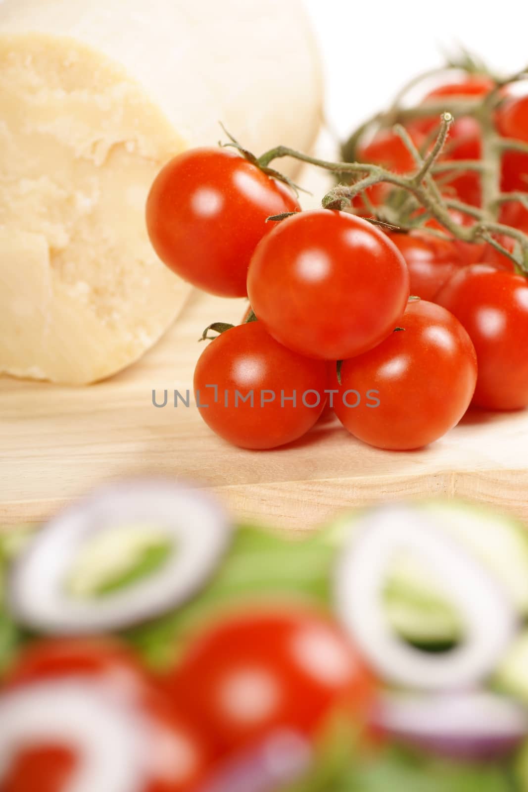 Food composition with ripe cherry tomatoes and parmesan cheese on a wooden cutting board. In the foreground a mixed salad. Selective focus on the background. Shallow DOF