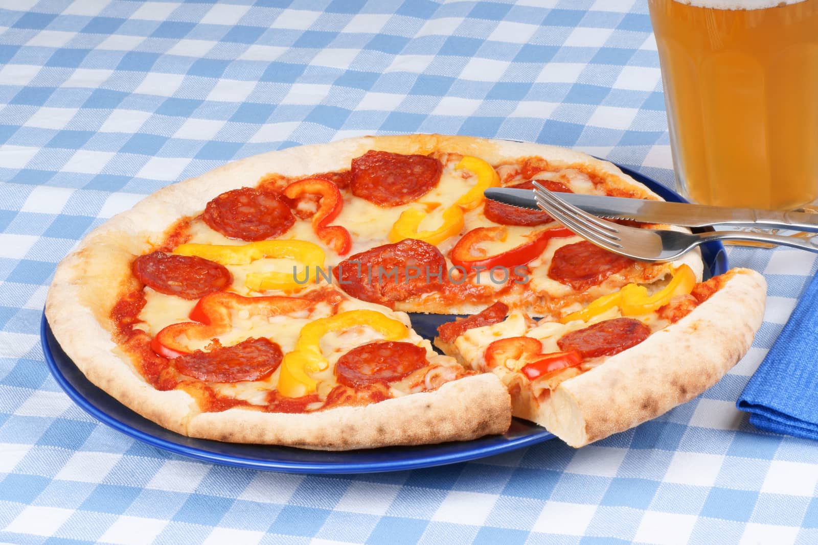 Set table with hot spicy pizza with salami and bell peppers and a glass of beer.